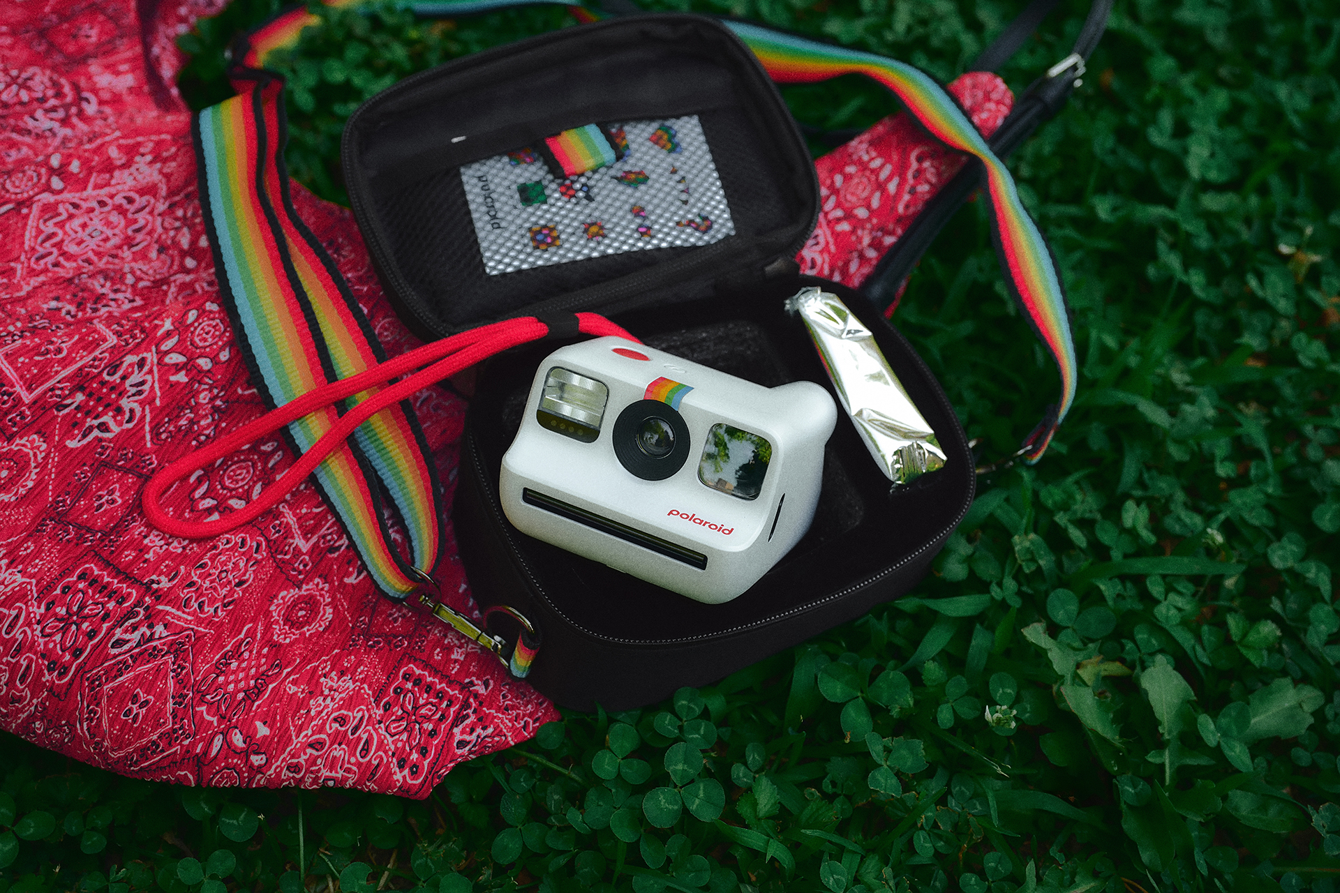 Beyaz bir Polaroid kamera yeşil çimlerin üzerinde siyah bir kılıfta duruyor.