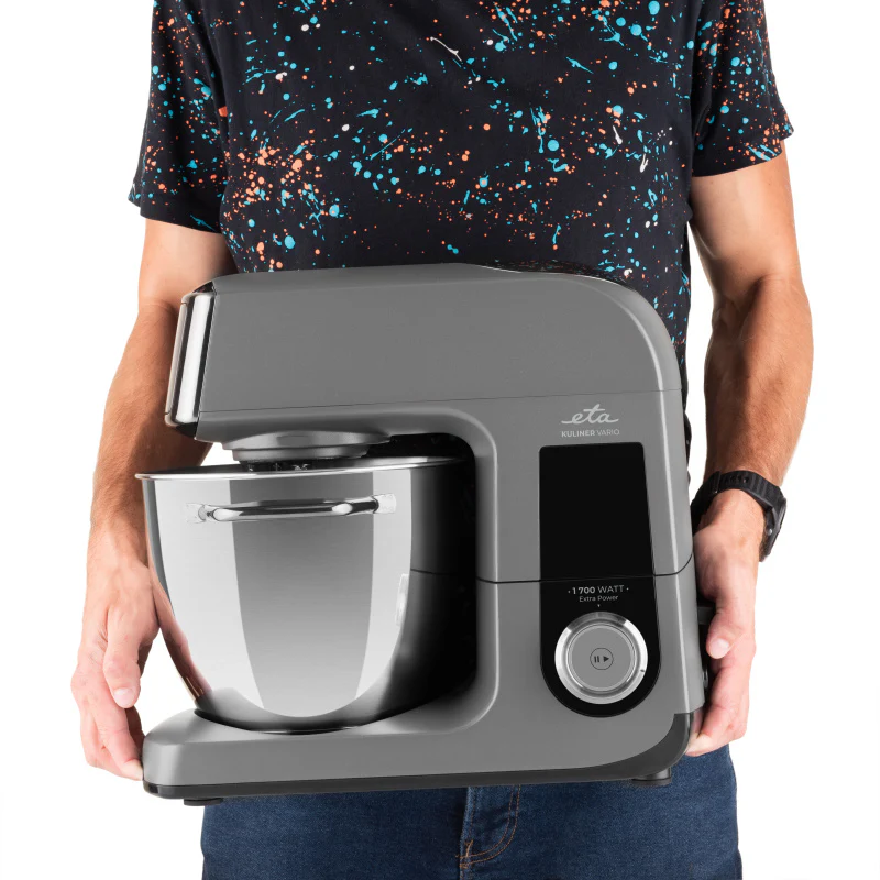 Szürke konyhai robotgép rozsdamentes acéltállal, személy tartja.