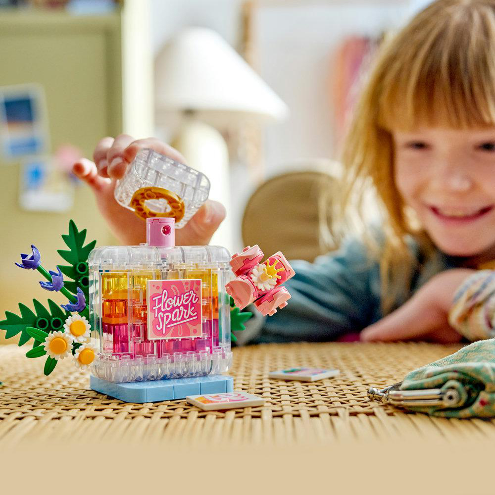 Ein Mädchen baut eine durchsichtige Parfümflasche aus bunten Legosteinen. Flower Spark-Etikett.