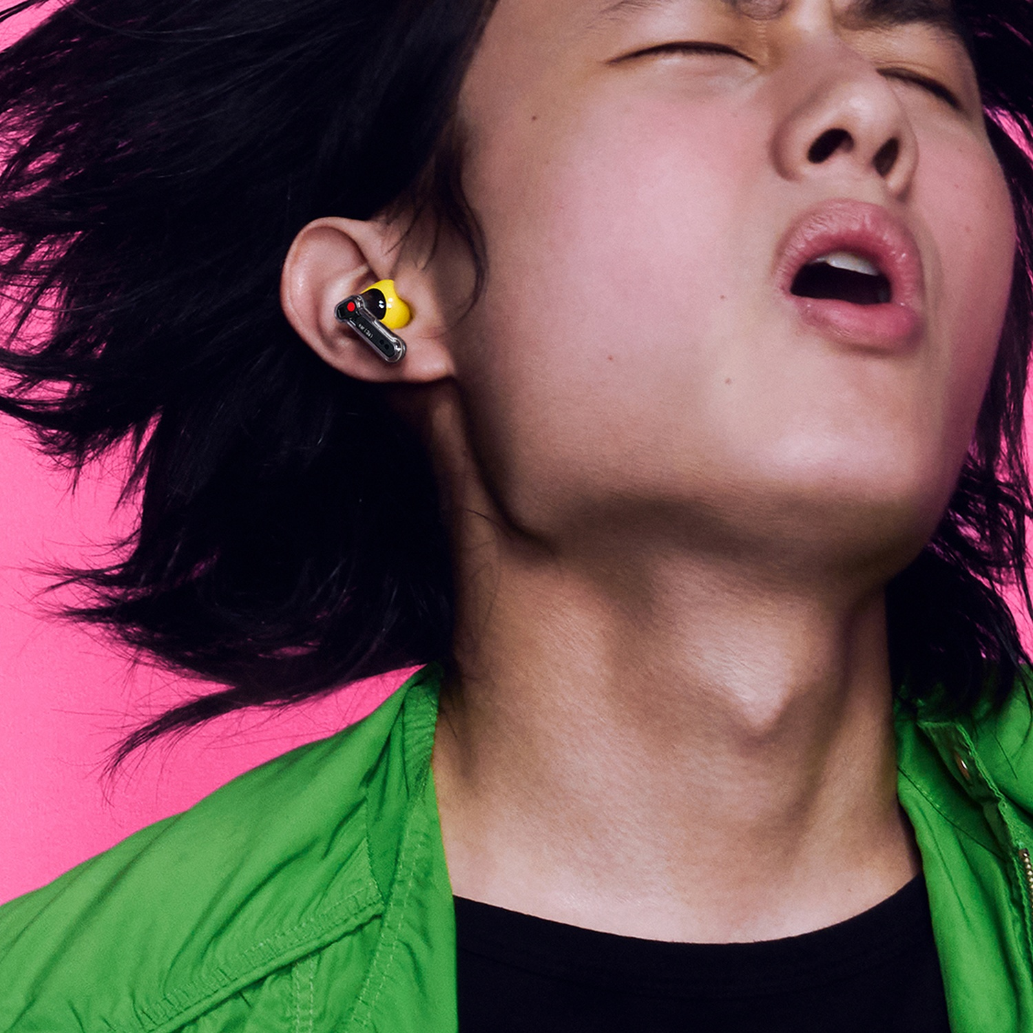Una persona con auricolare giallo nell'orecchio, su sfondo rosa.