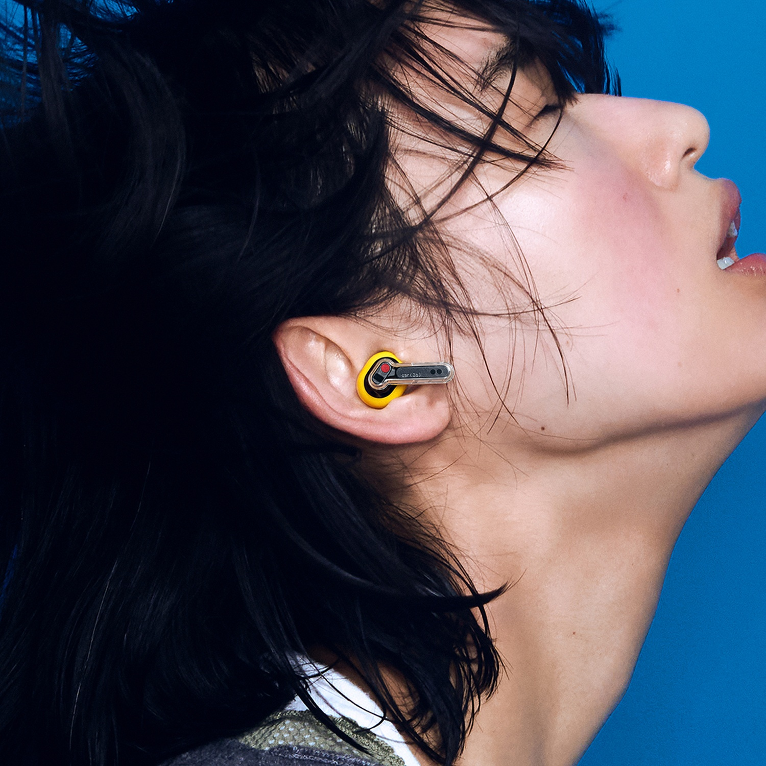 Profilato di una persona con capelli neri che indossa un auricolare giallo su sfondo blu.