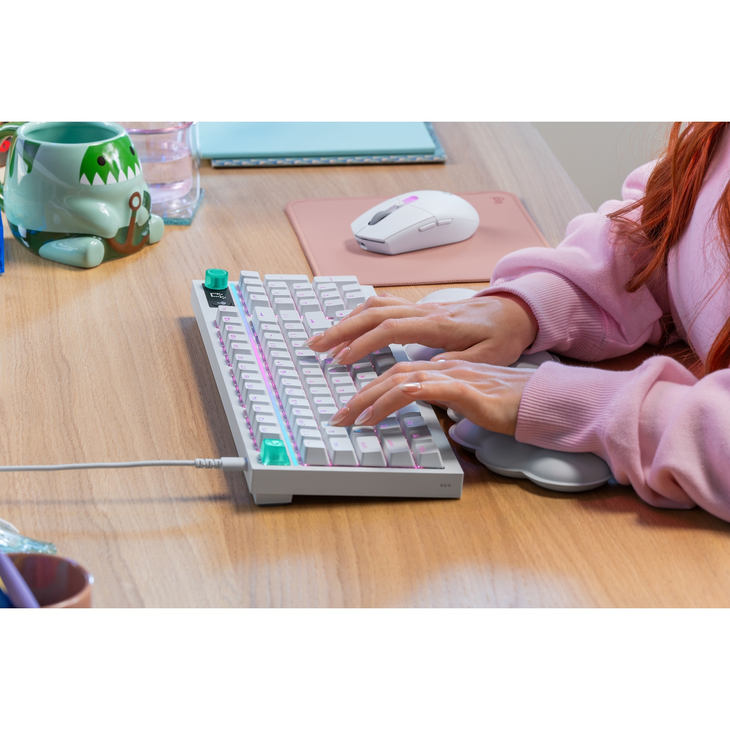 Una persona digita su una tastiera bianca con illuminazione RGB, accanto un mouse.