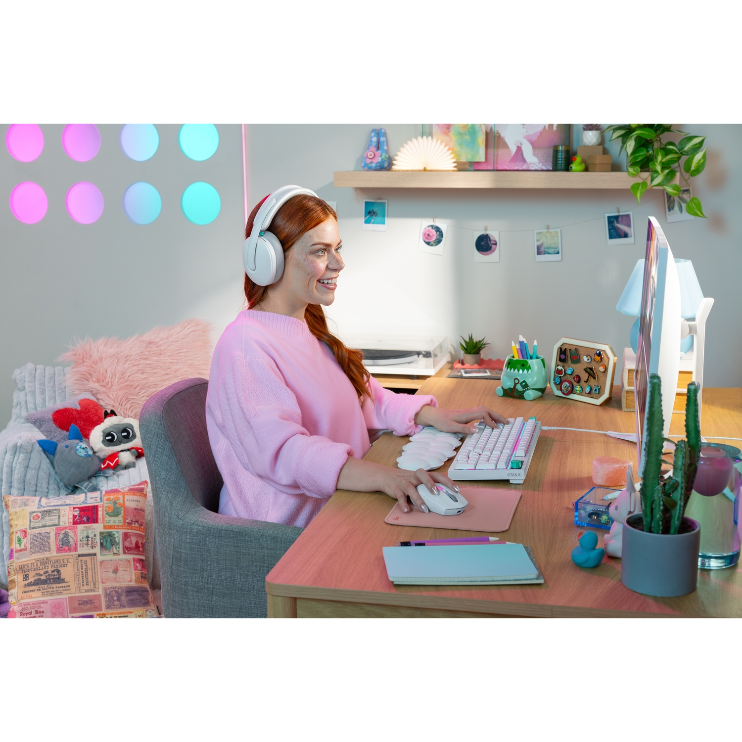 Donna con cuffie sorride al computer, scrivania con tastiera, mouse, piante e decorazioni.
