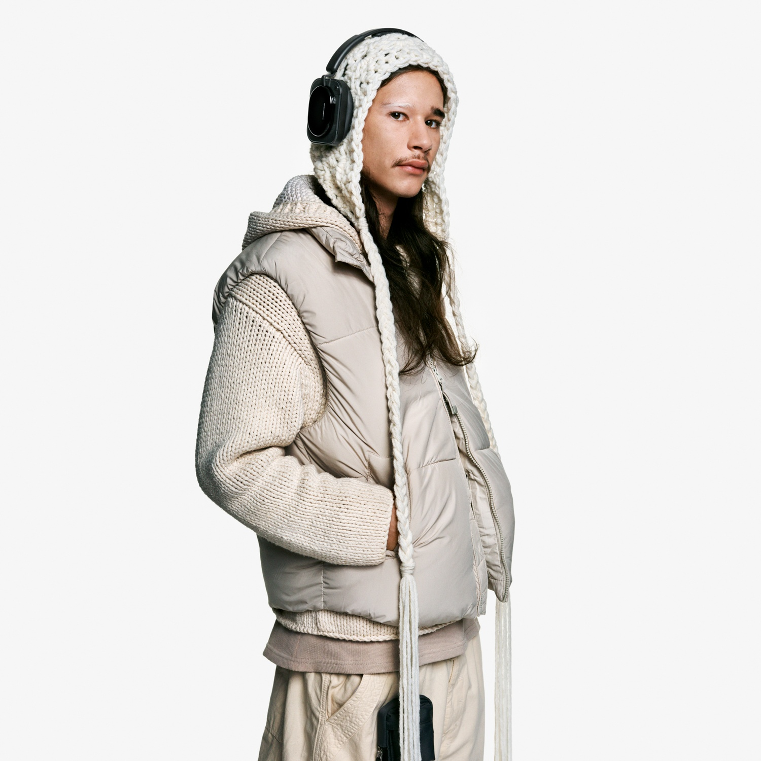 Uomo con cuffie e cappello di lana, gilet imbottito su maglione di lana.