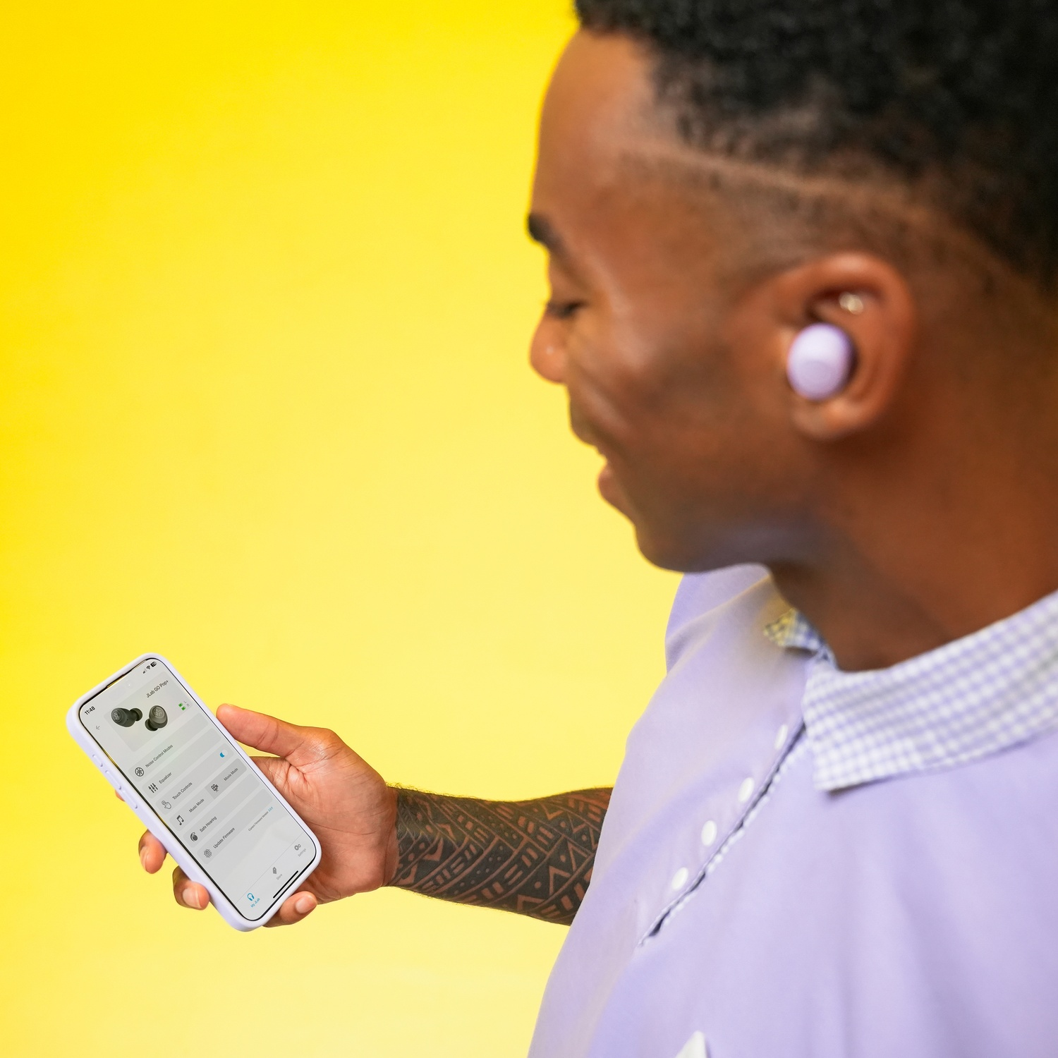 Homme avec écouteurs violets et téléphone sur fond jaune.