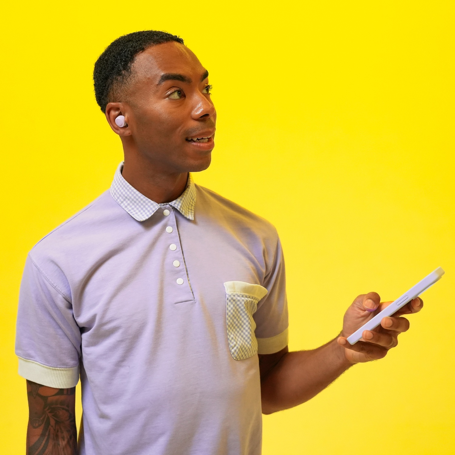 Homme en polo violet avec écouteurs tient téléphone sur fond jaune vif.