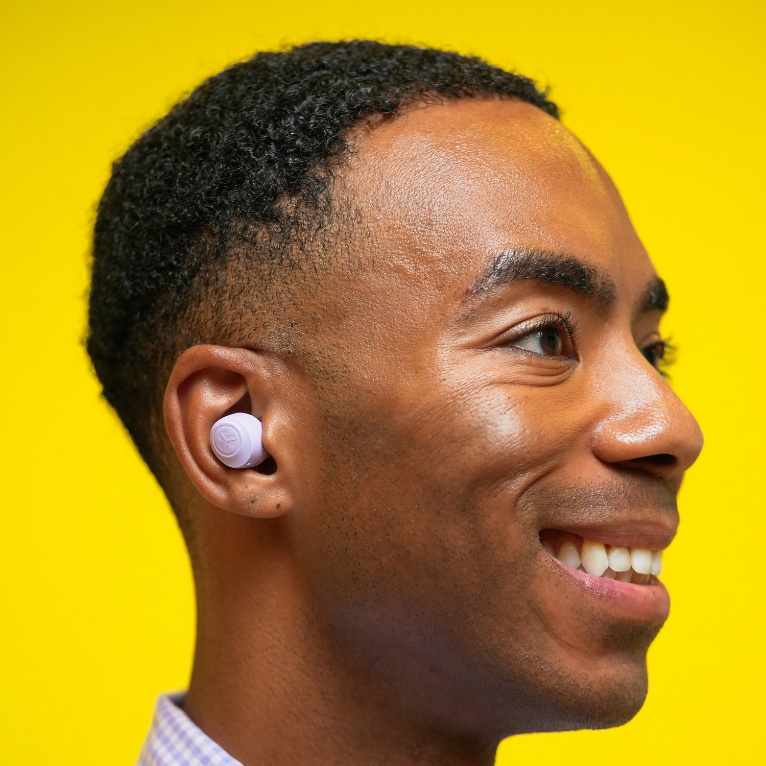 Homme avec un écouteur violet dans l'oreille, souriant sur fond jaune.