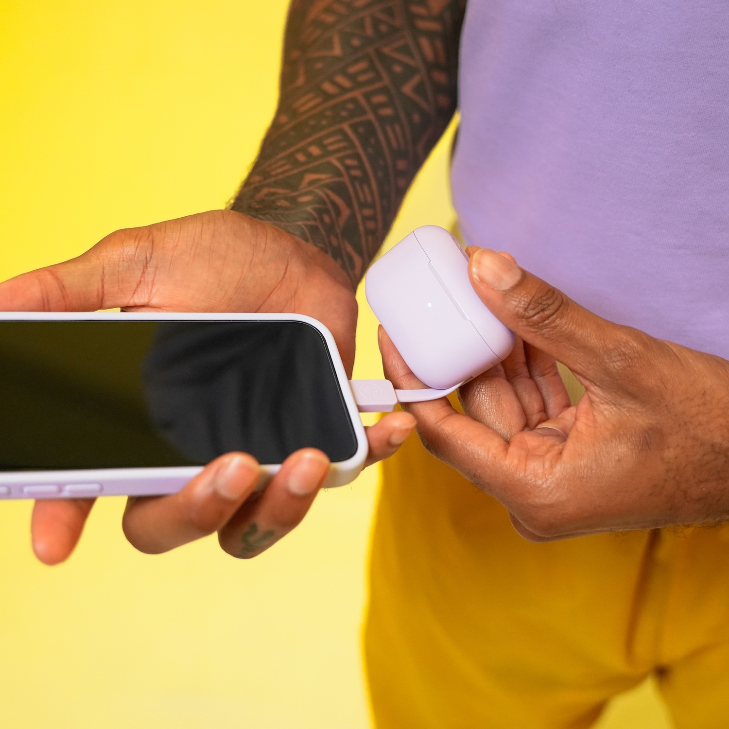 Une personne tatouée charge un étui violet clair avec un câble connecté à un téléphone.