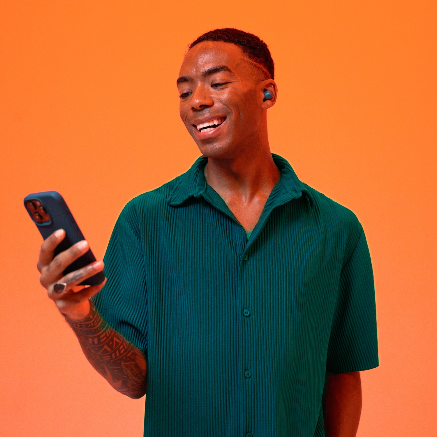Un homme portant des écouteurs et tenant un téléphone sur fond orange.