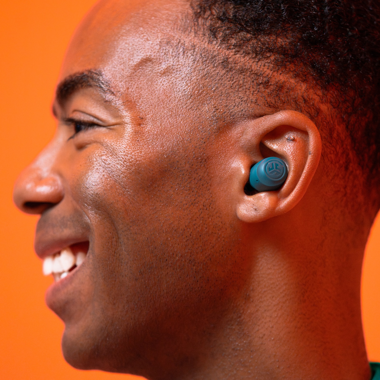 Un homme avec un écouteur bleu dans l'oreille sur fond orange.