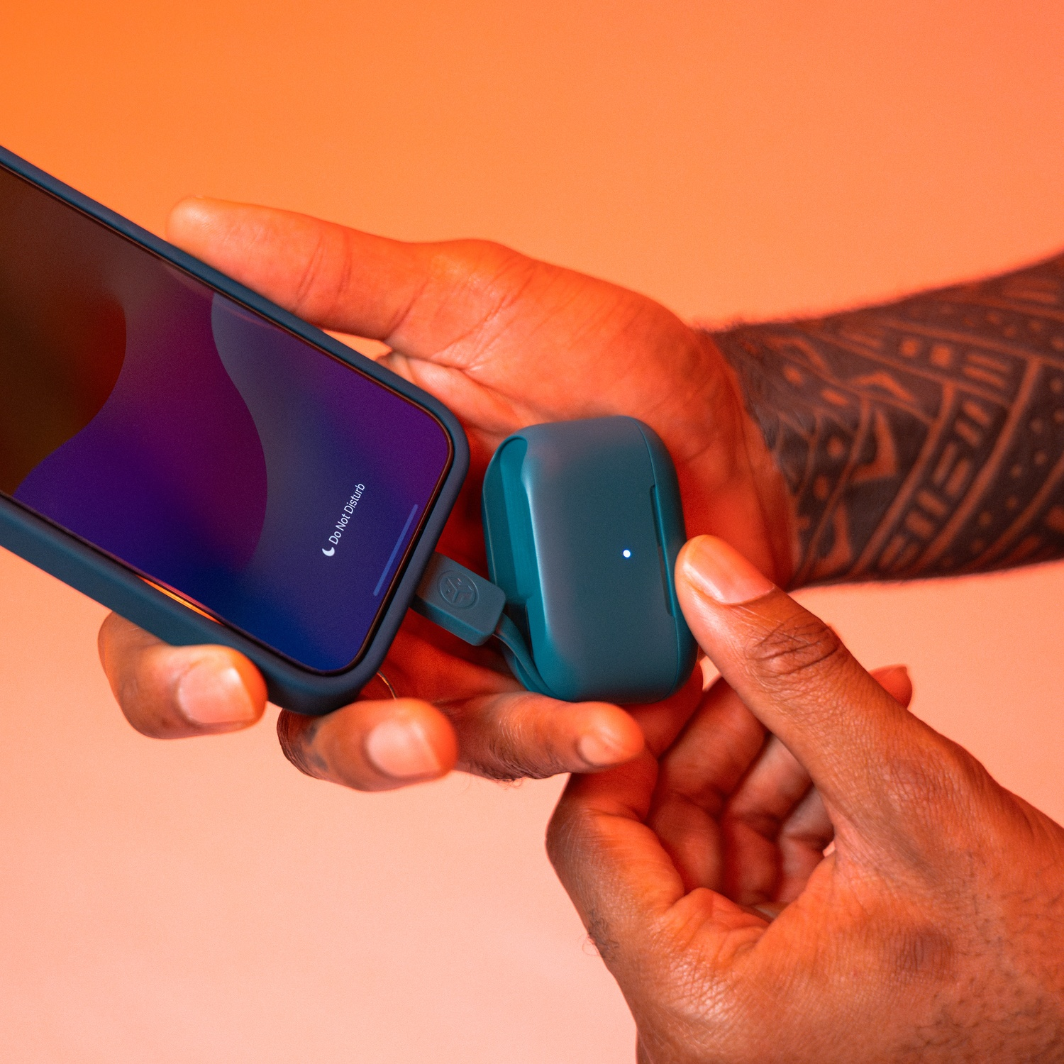 Des mains tiennent un smartphone et un étui de chargement bleu sarcelle pour écouteurs. Un câble les relie.