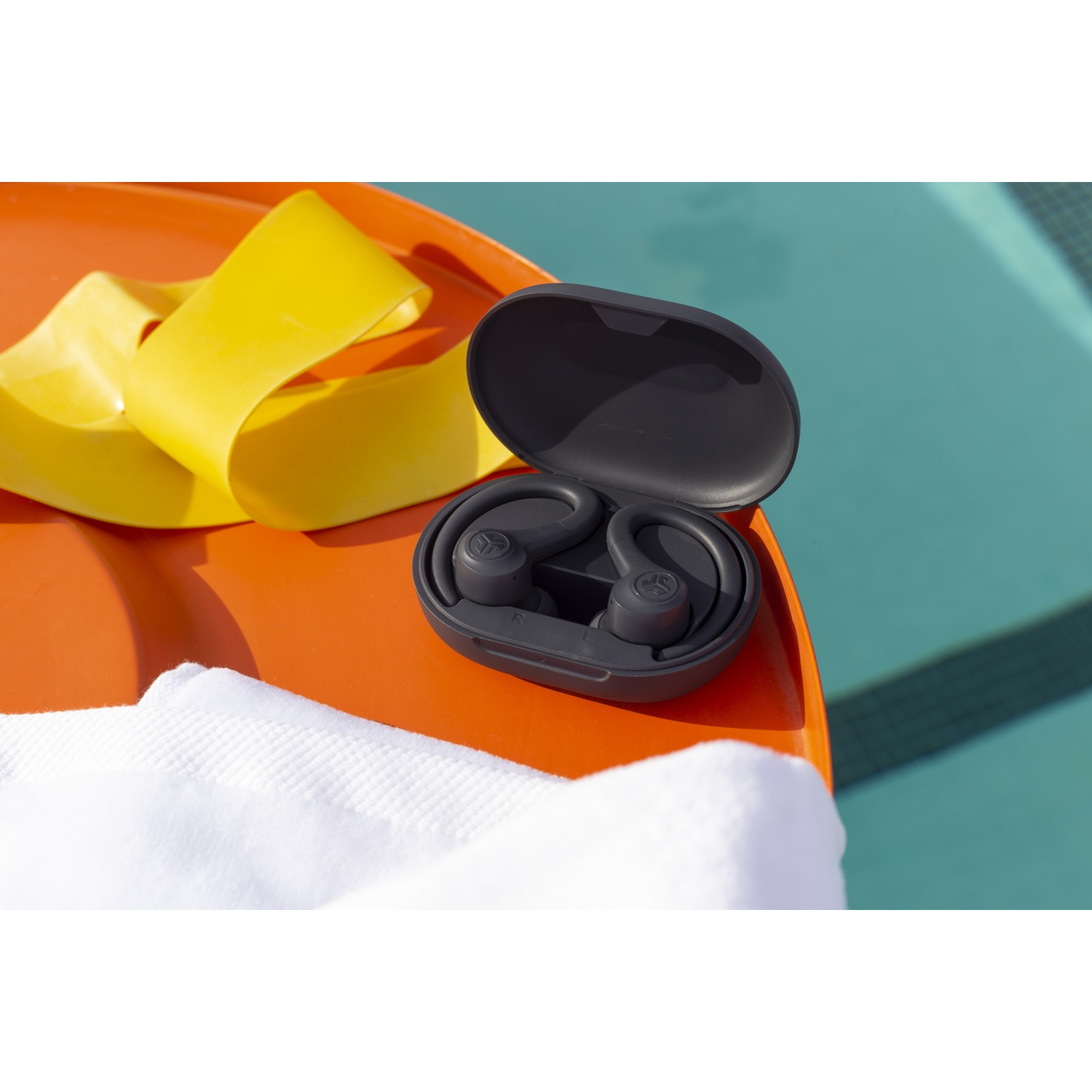 Gray earbuds in charging case on orange tray with yellow band and towel.