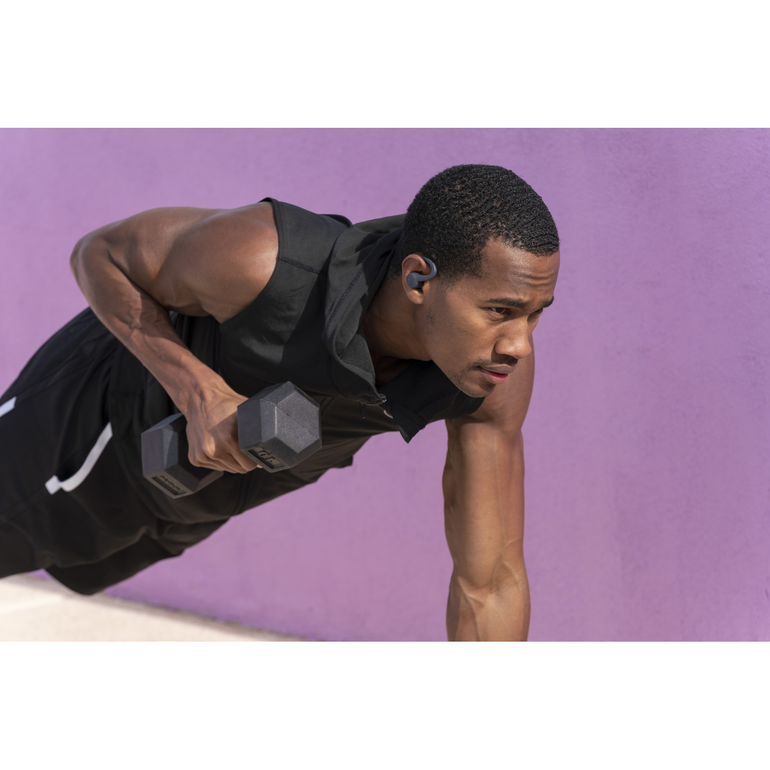 Man in black workout clothes does a dumbbell row in a plank position.