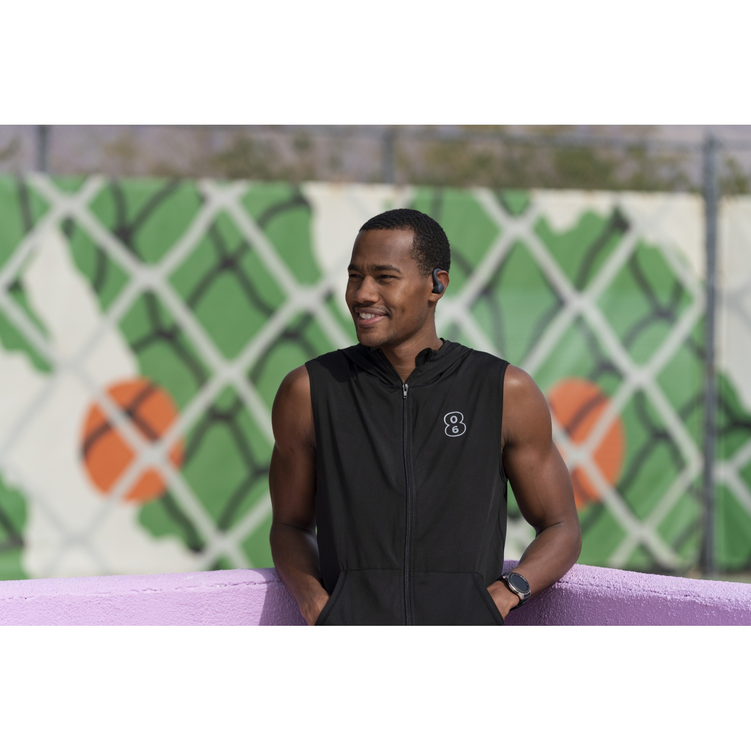 A man with headphones smiles in front of a wall with basketball art.