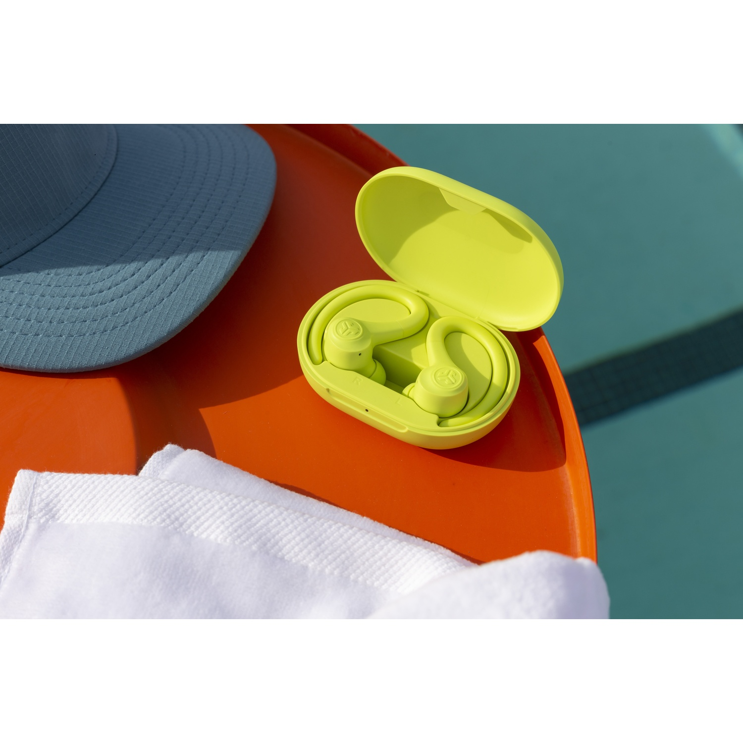 Neon gele oordopjes in een hoesje op een oranje tafel naast een blauwe pet en een witte handdoek.