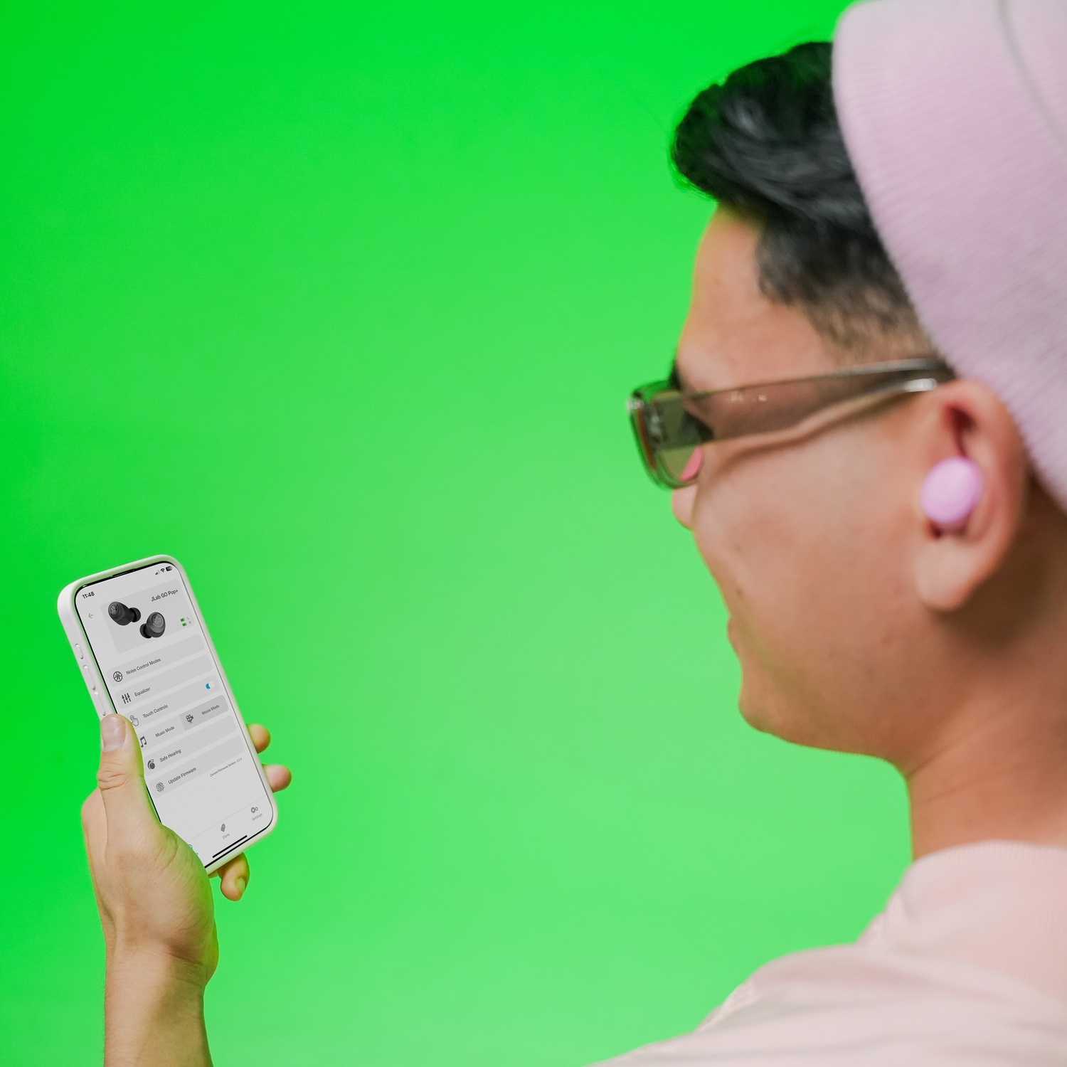 Personne bonnet rose lunettes soleil tient téléphone affiche app écouteurs fond vert.