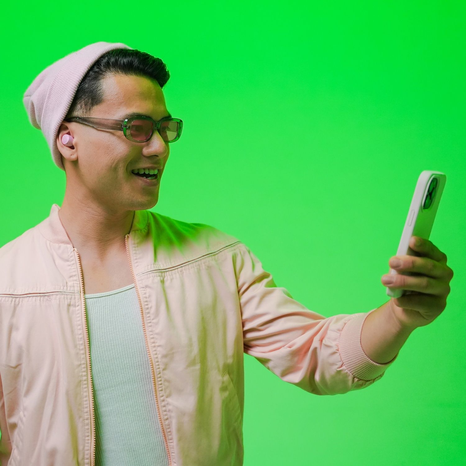 Un homme portant un bonnet rose et des lunettes de soleil tient un téléphone, avec des écouteurs roses.