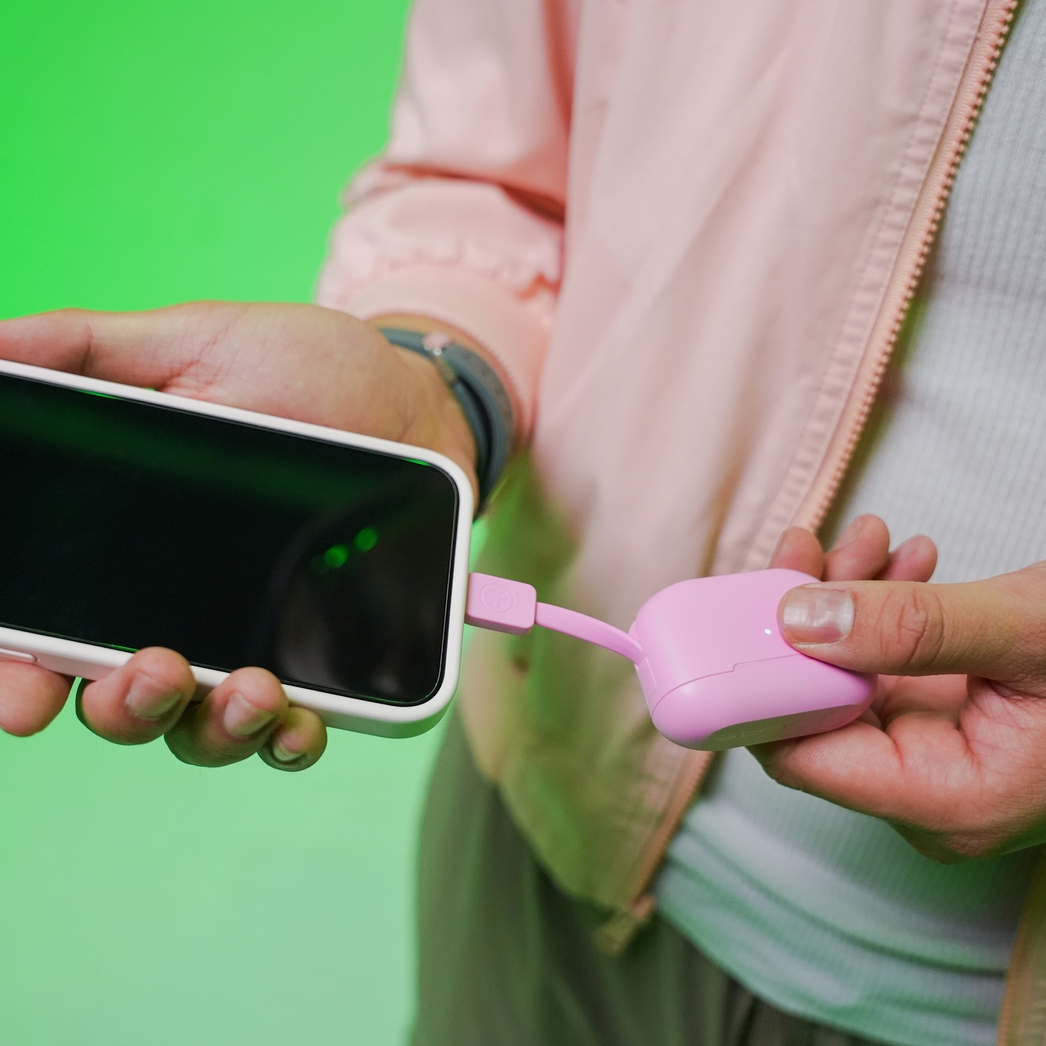 Une main tient un smartphone pendant qu'une autre branche un câble de chargement rose.