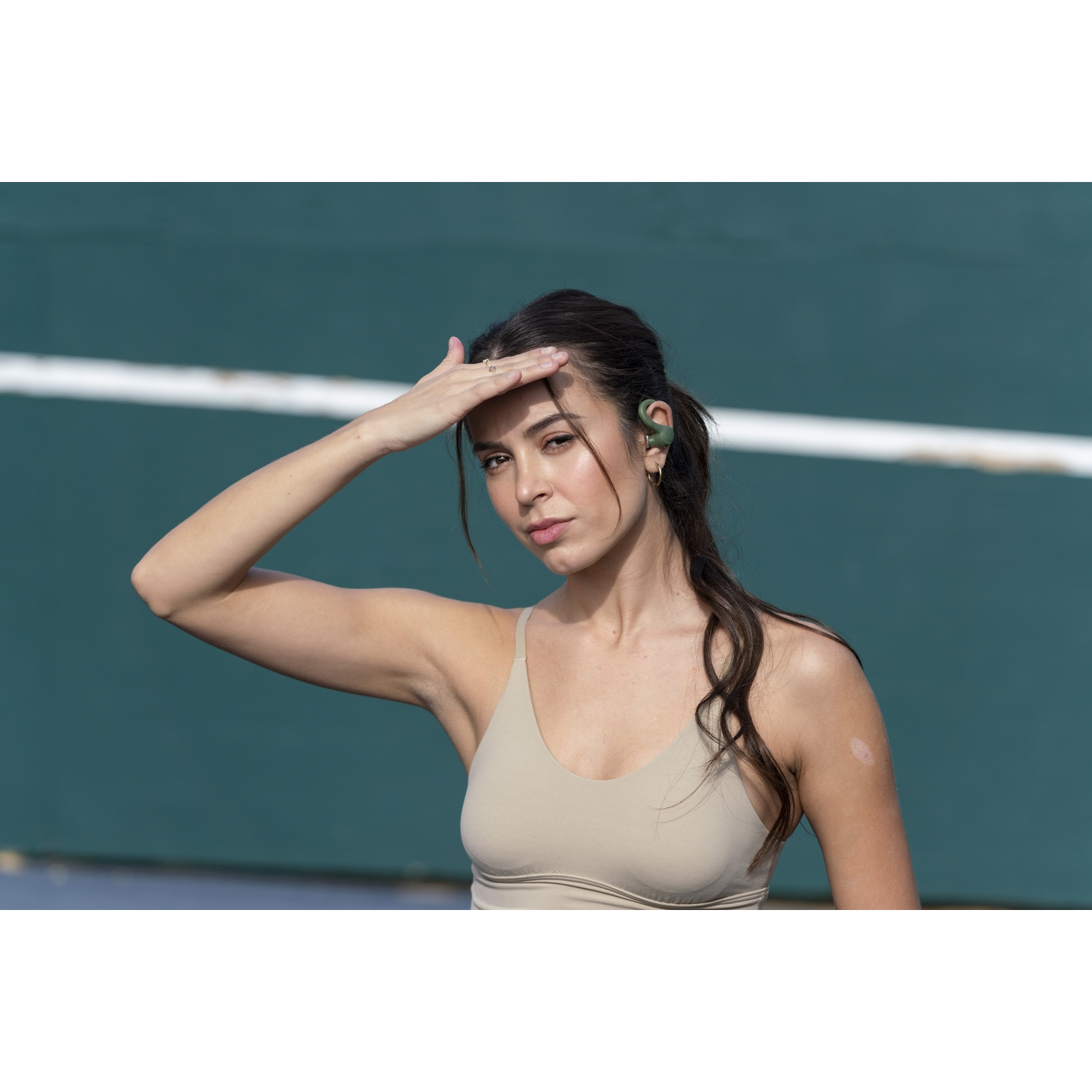 Vrouw in beige sportbeha en oordopjes kijkt in de verte.