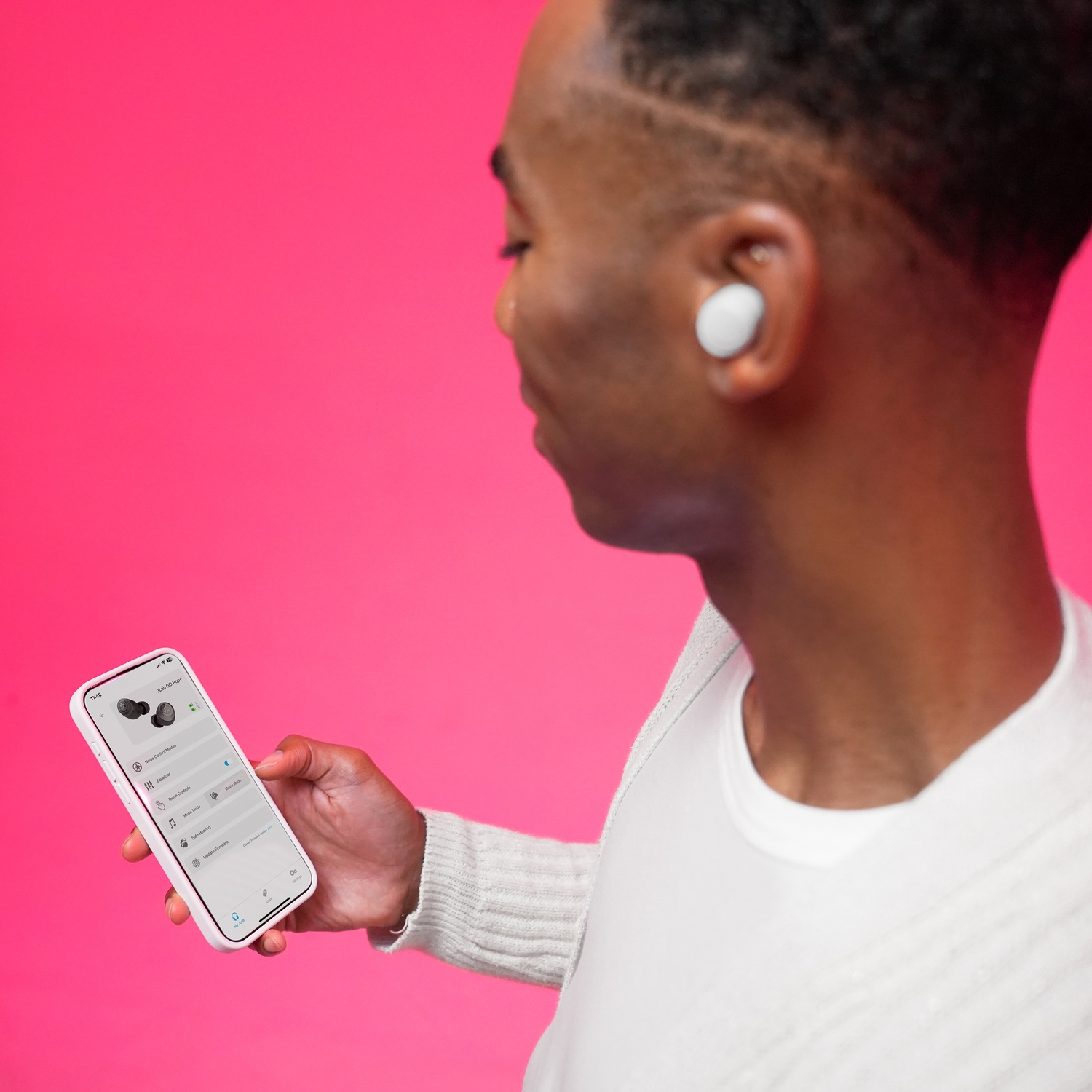 Man in white shirt uses phone with earbuds app. Pink background.