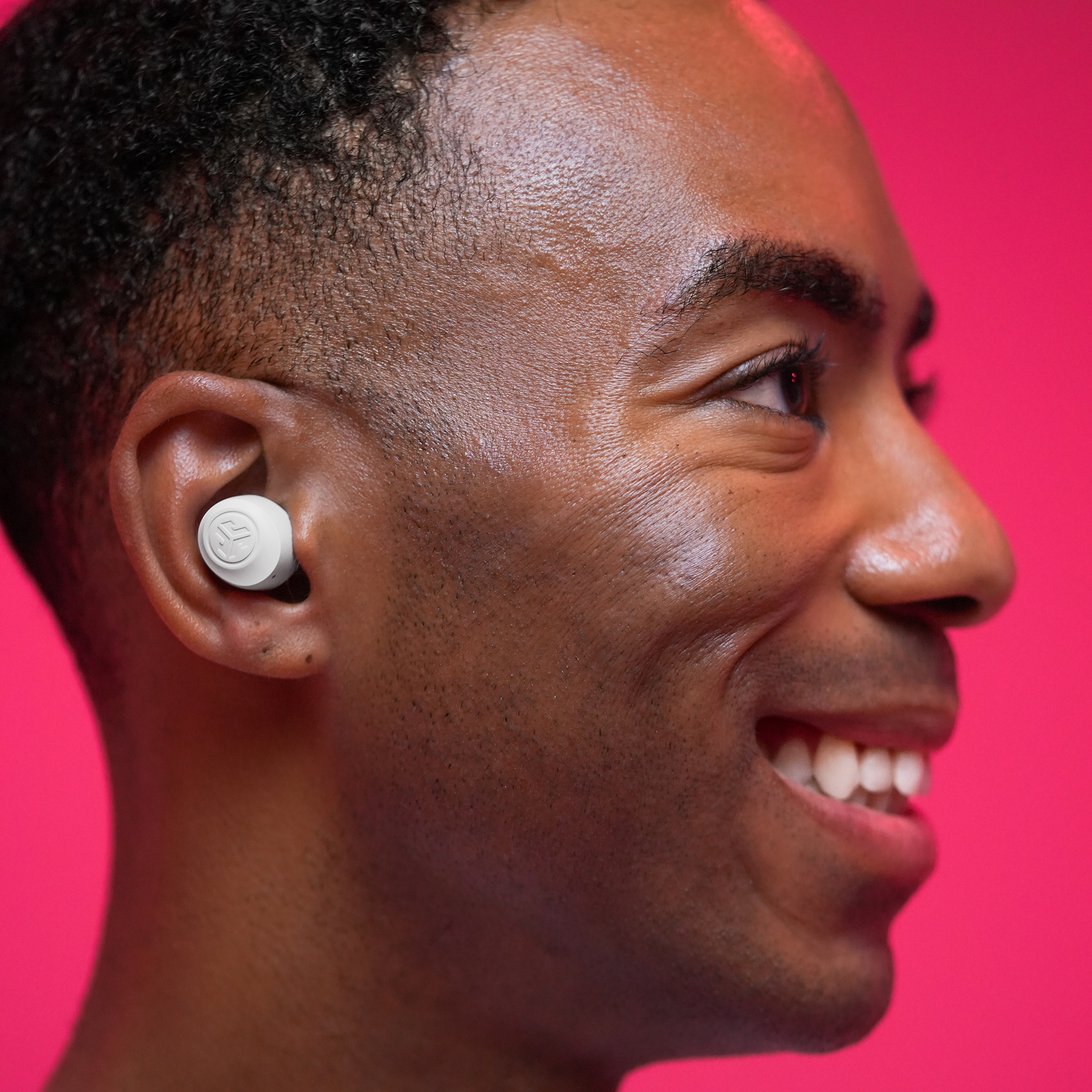 Man wearing white earbuds against a pink background.