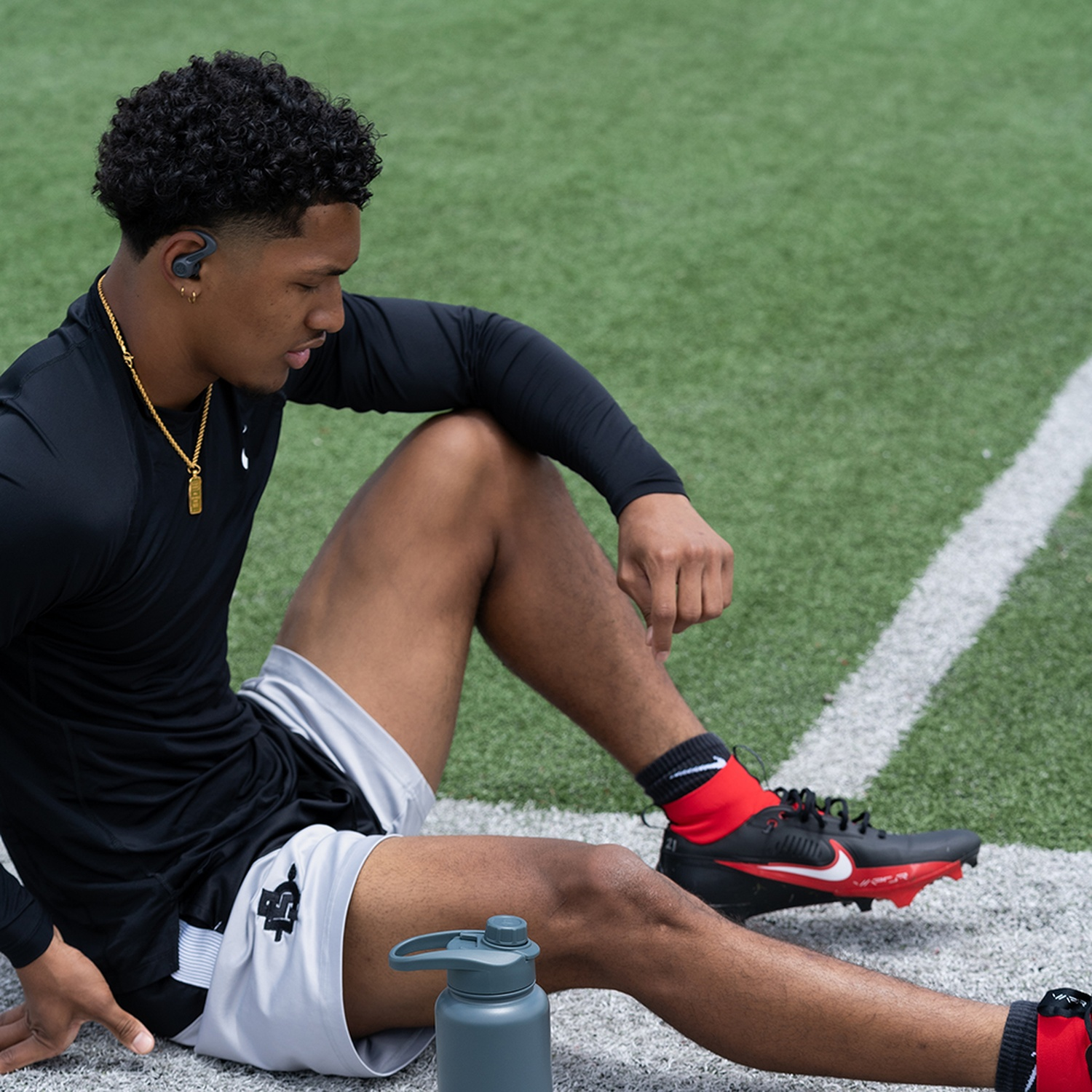 A man sits on a football field wearing earbuds.