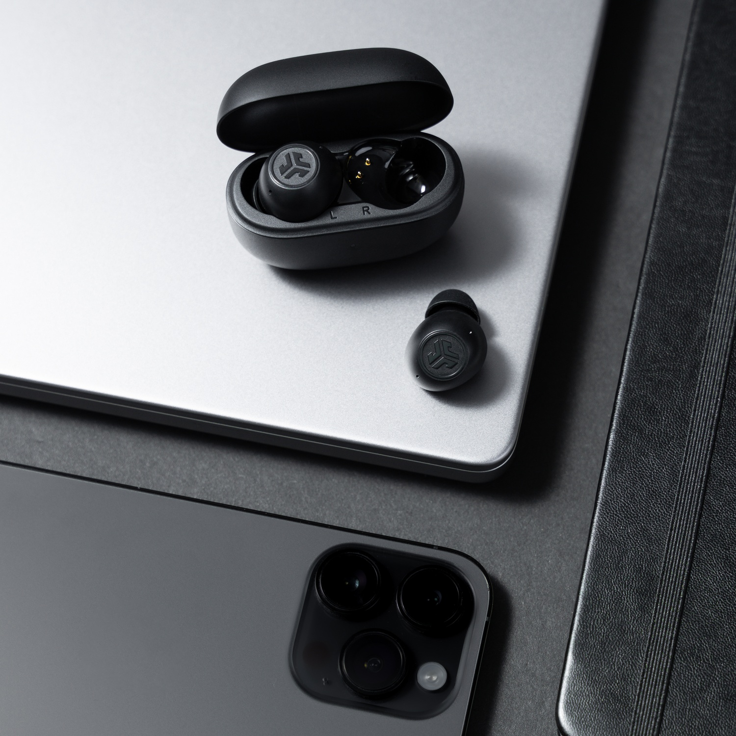 Zwarte oordopjes met oplaadcase liggen op laptop naast smartphone.