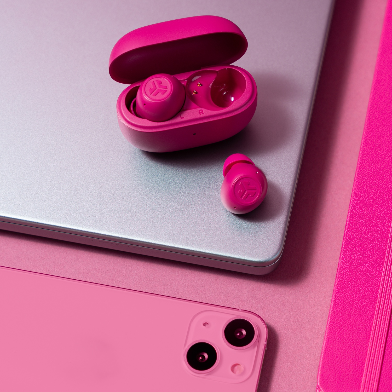 Roze oordopjes en hoesje op een laptop, met een roze telefoon en notitieboek.