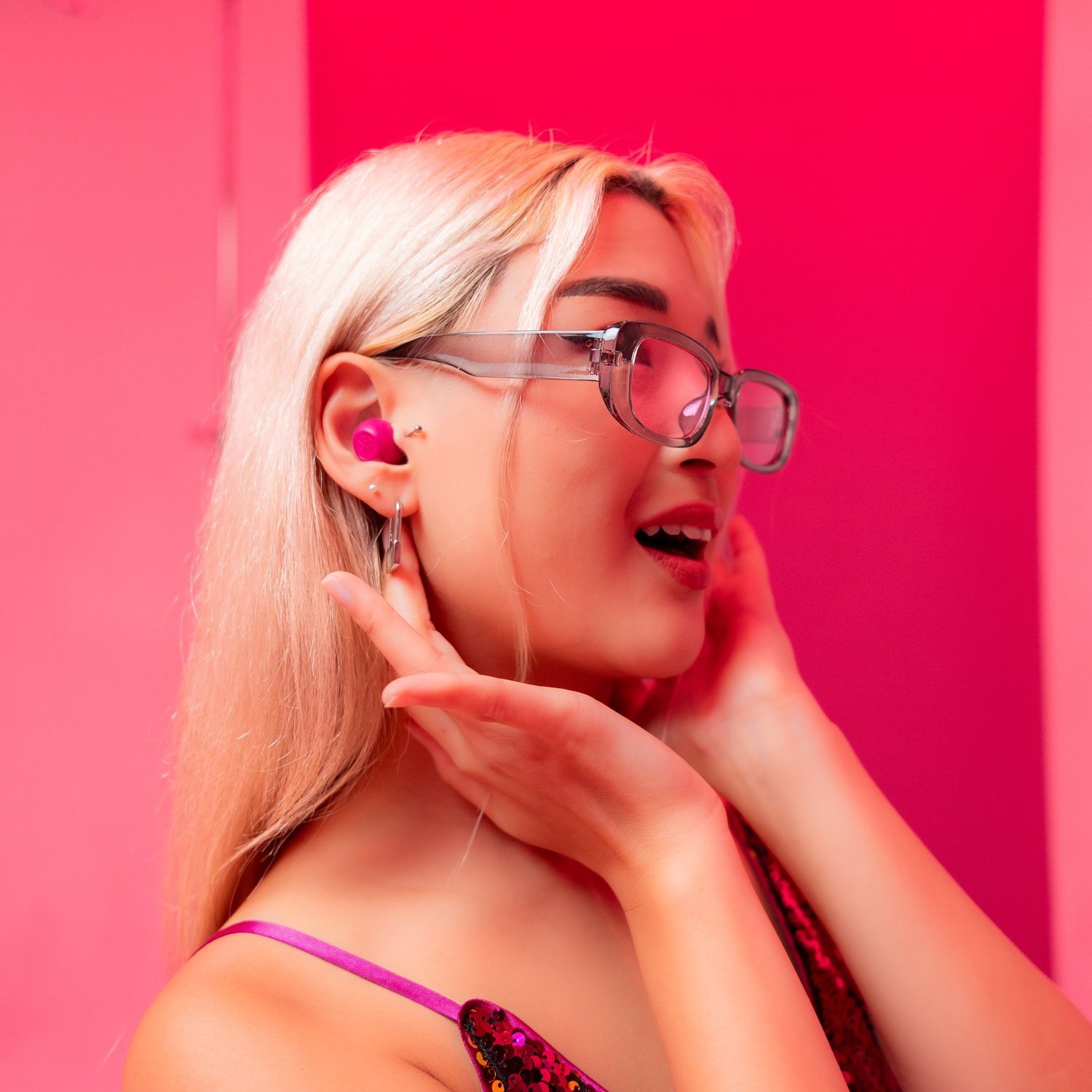 Een blonde vrouw met bril en roze oordopjes. Roze achtergrond.