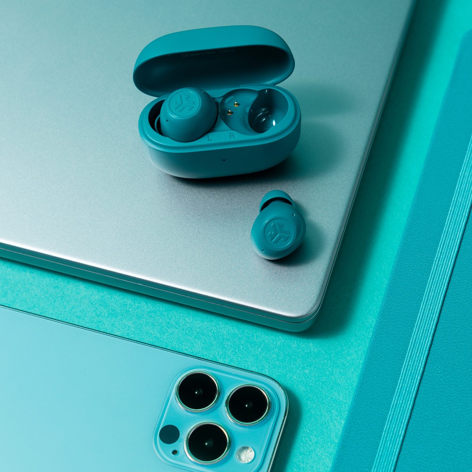 Turquoise oordopjes in hoesje op laptop naast telefoon en notitieboek.