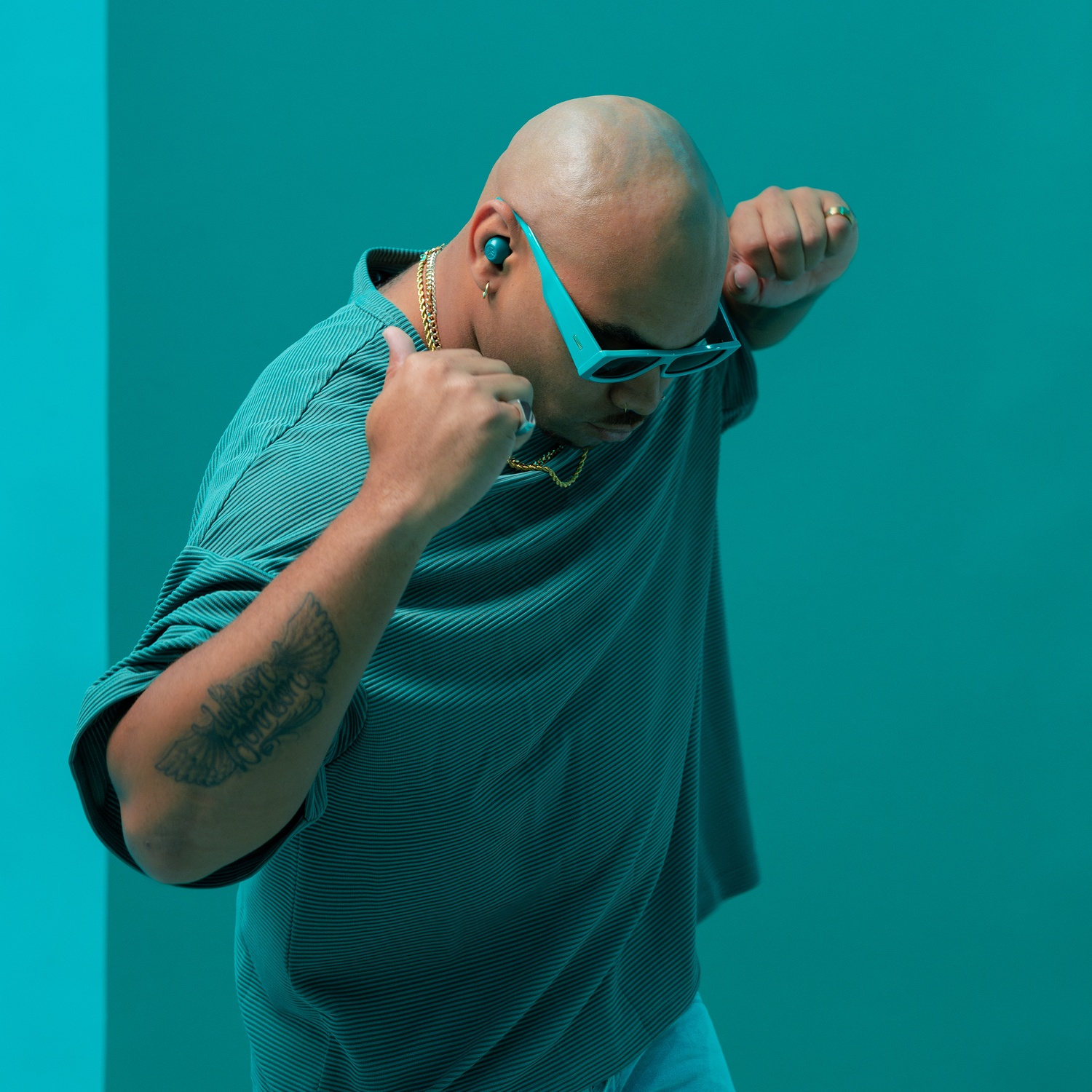 Een kale man in een turquoise hemd en zonnebril danst.