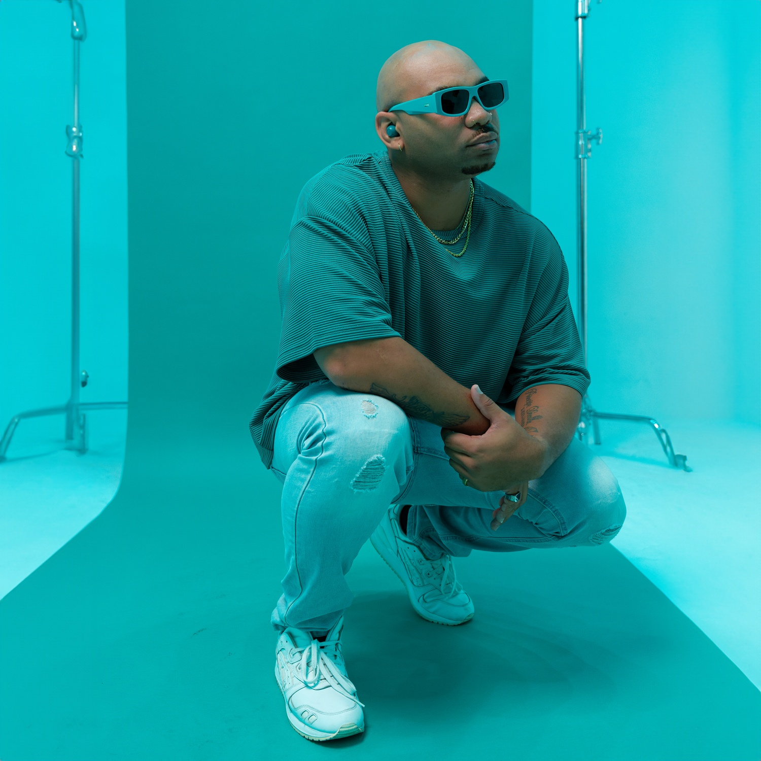 Een man in een spijkerbroek en gestreept shirt hurkt op een turquoise achtergrond.