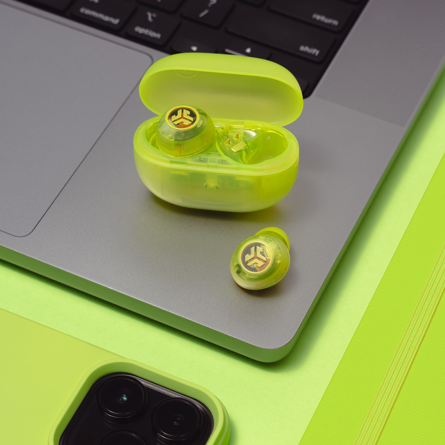 Neongele oordopjes in een transparante oplaadcase liggen op een laptop.