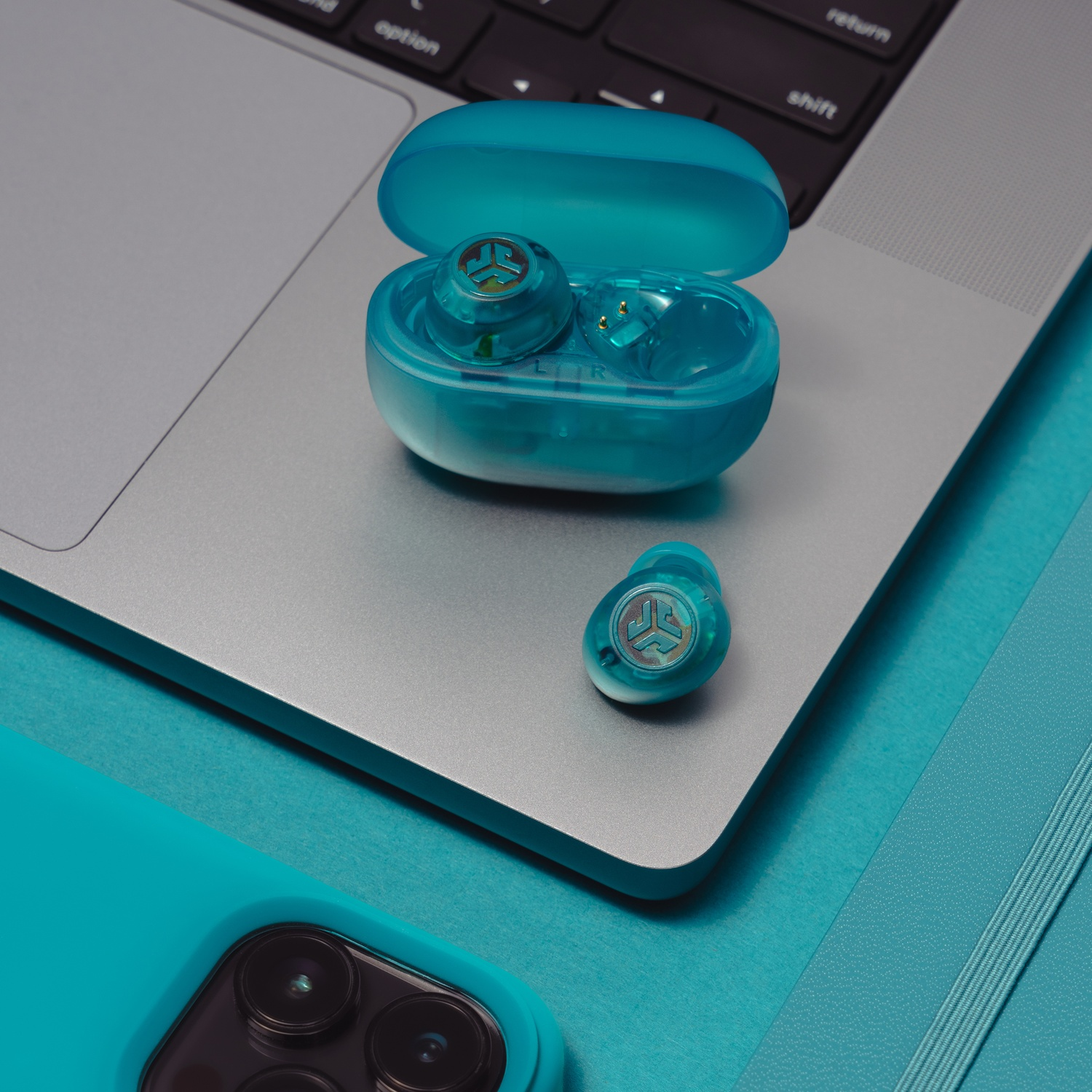 Turquoise oordopjes en hoesje op een laptop naast een telefoon en notitieboek.