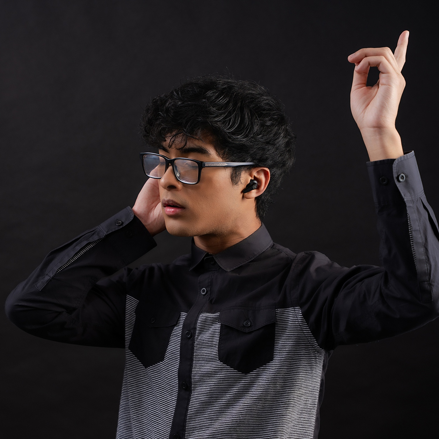 Jeune homme lunettes et écouteurs, chemise rayée noir et blanc, lève la main.