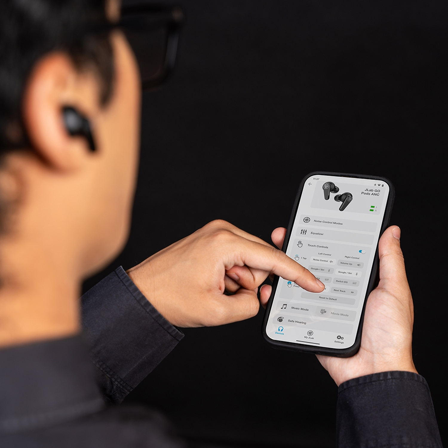Homme avec lunettes utilise une application mobile pour les écouteurs. Fond noir.