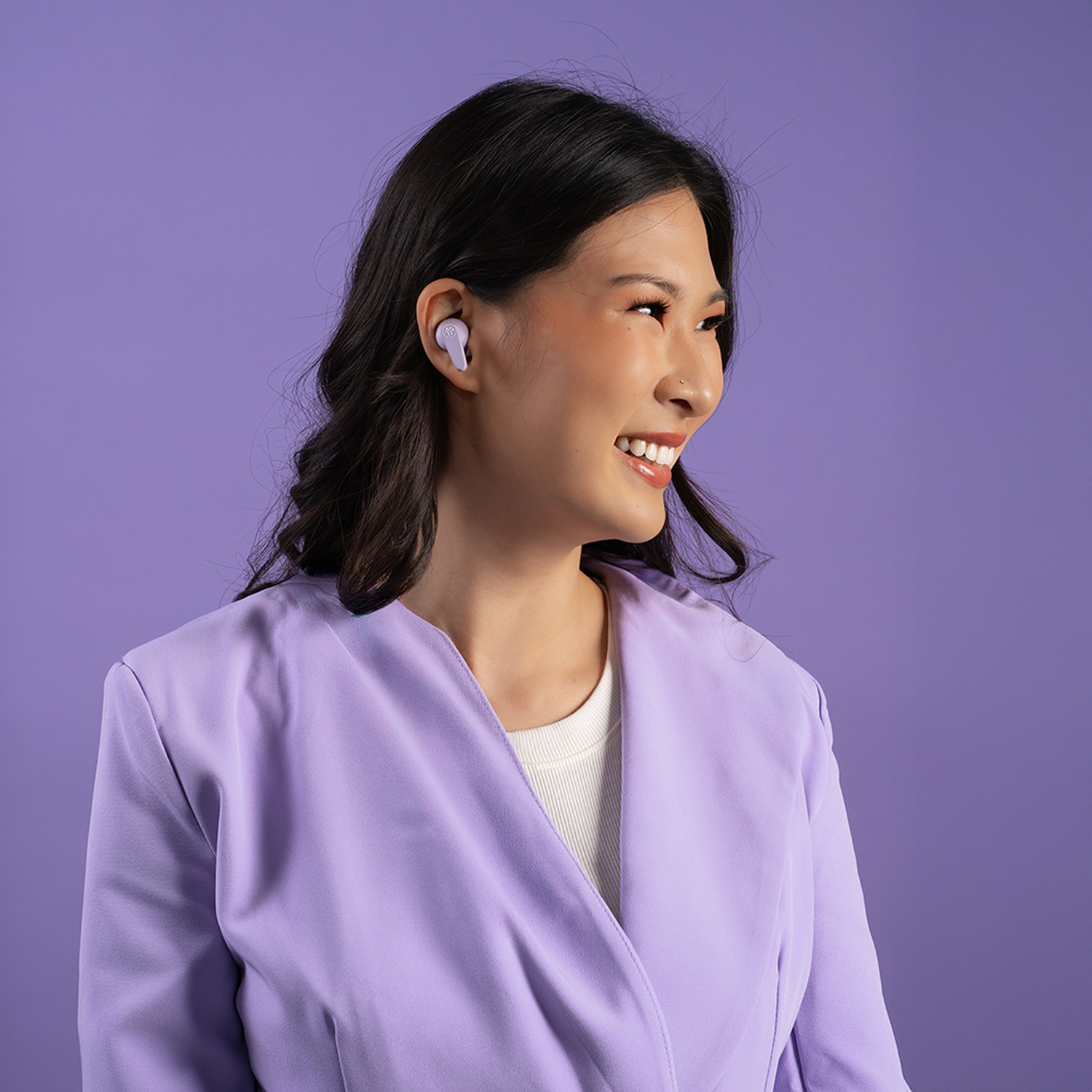 Une femme en blazer violet et écouteurs sourit.