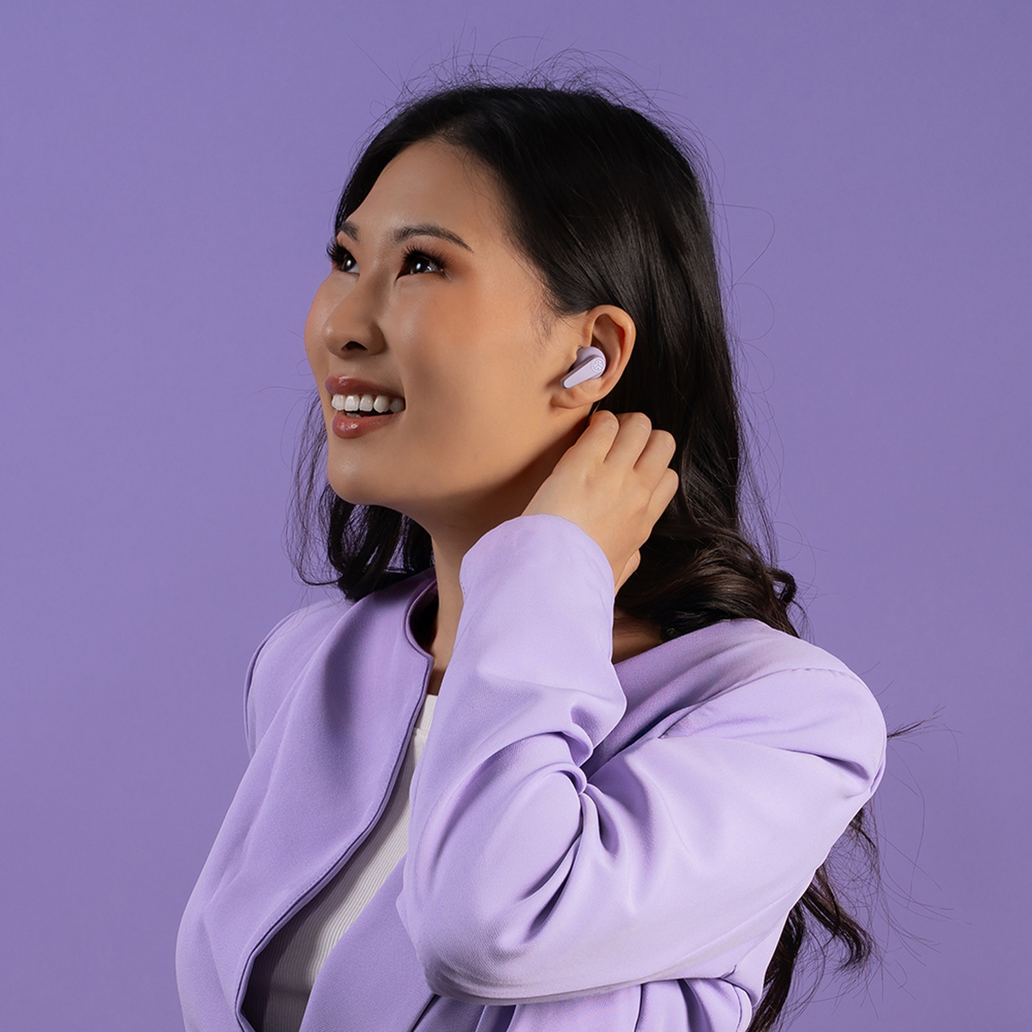 Une femme en blazer violet porte des écouteurs et regarde en l'air, souriante.