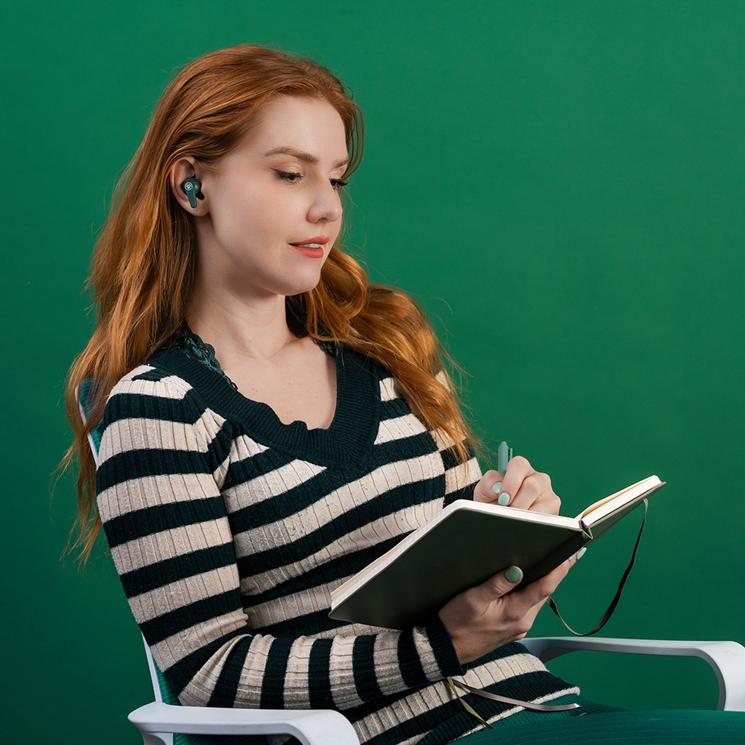 Une rousse avec des écouteurs écrit dans un carnet.