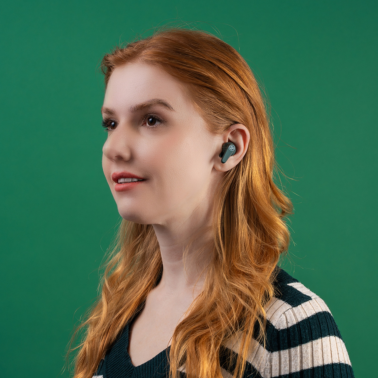 Femme aux cheveux roux portant des écouteurs sur fond vert.