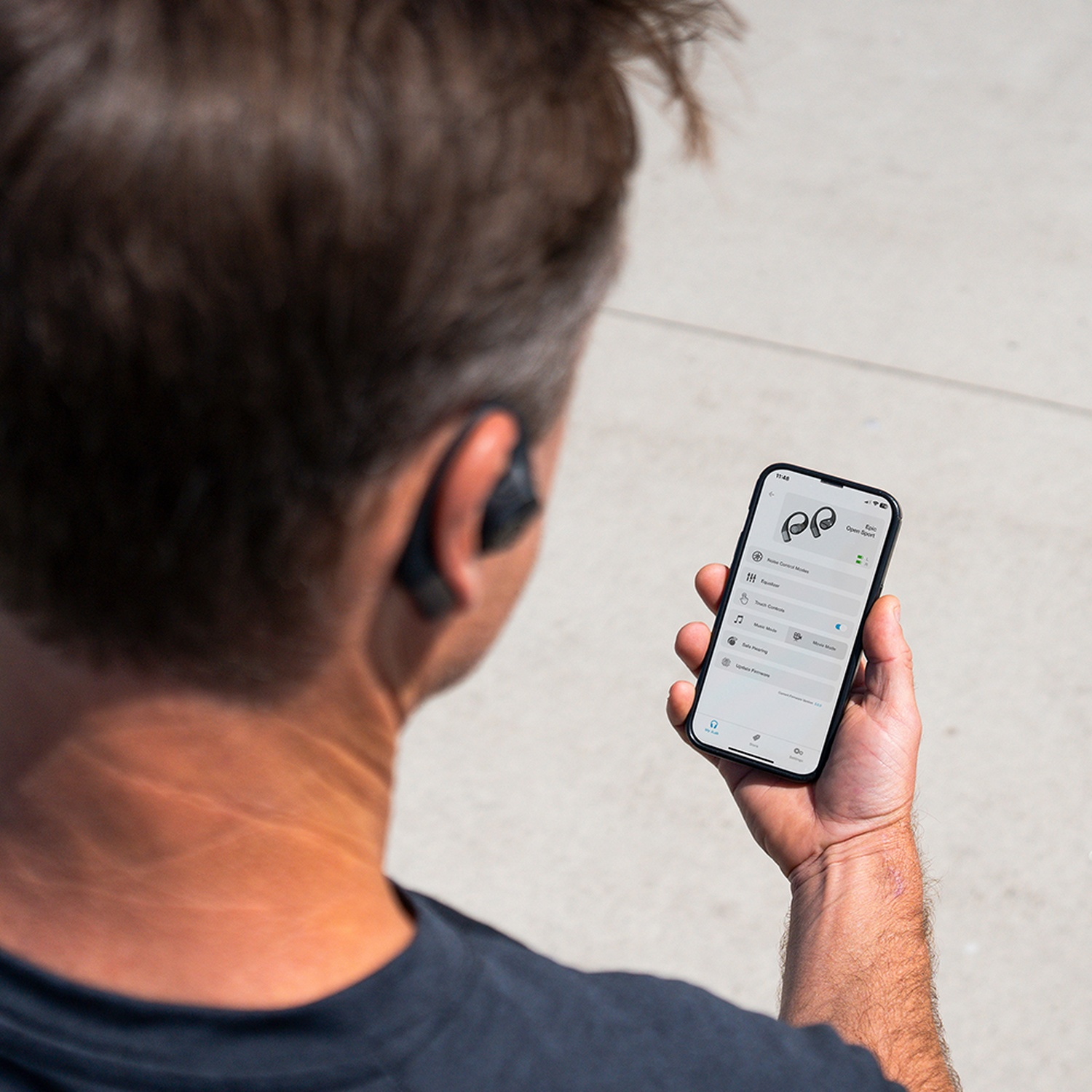 Een man houdt een smartphone met een koptelefoon-app vast. De achterkant van zijn hoofd is zichtbaar.