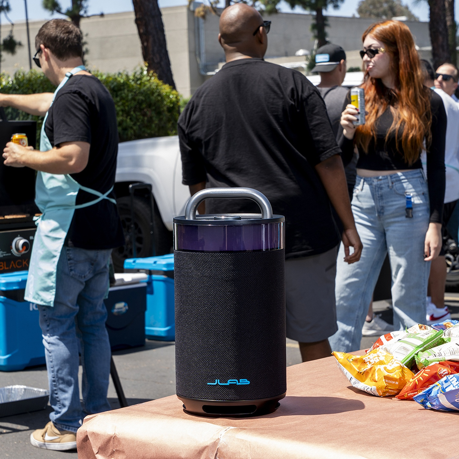 A black speaker sits on a table with chips. People are in the background.