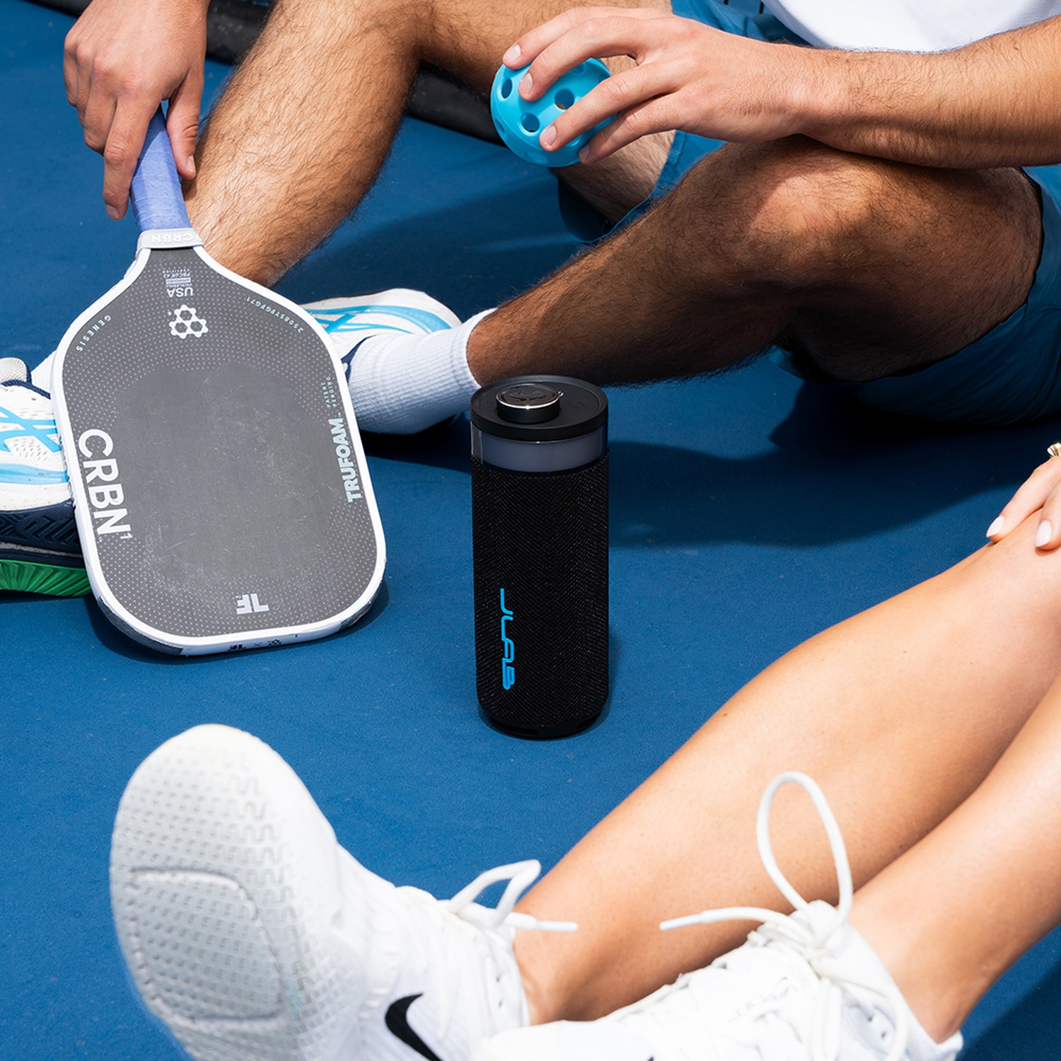 People with pickleball paddle, ball, and speaker on blue court.