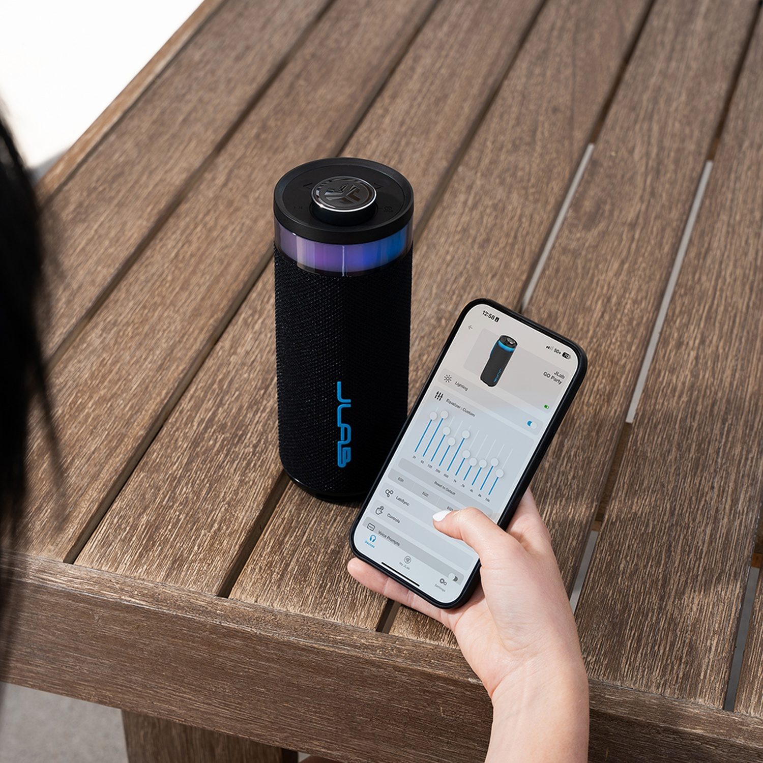 Black speaker with light effects and smartphone app on a wooden table.