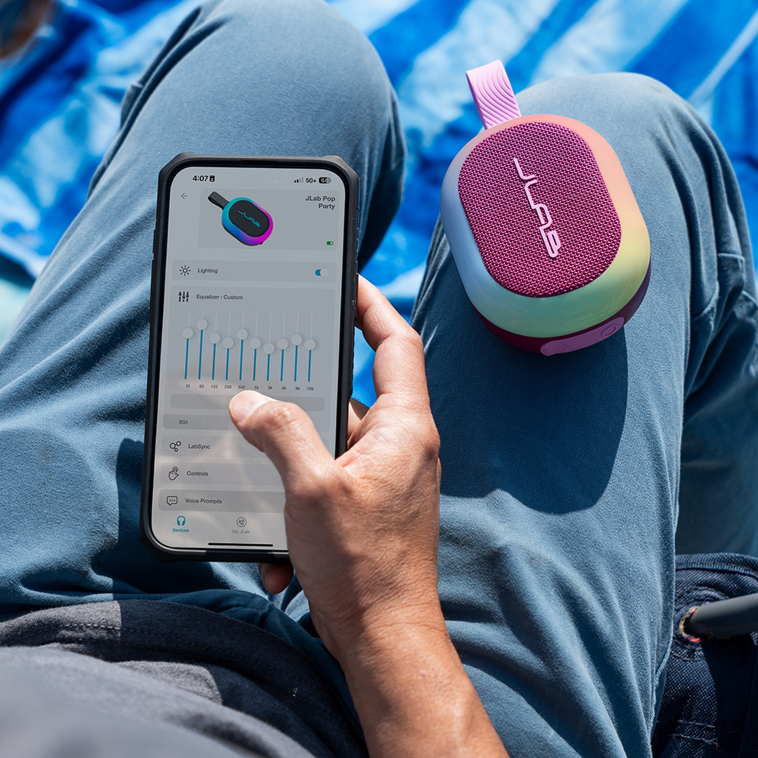 Person holding phone showing EQ settings next to a colorful speaker on lap.