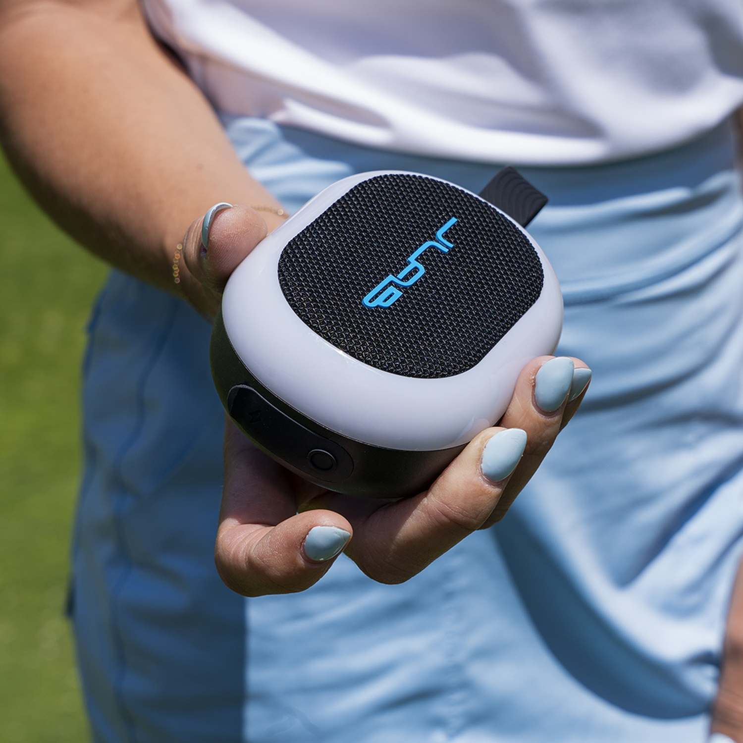 A hand holds a white and black speaker with a blue logo.