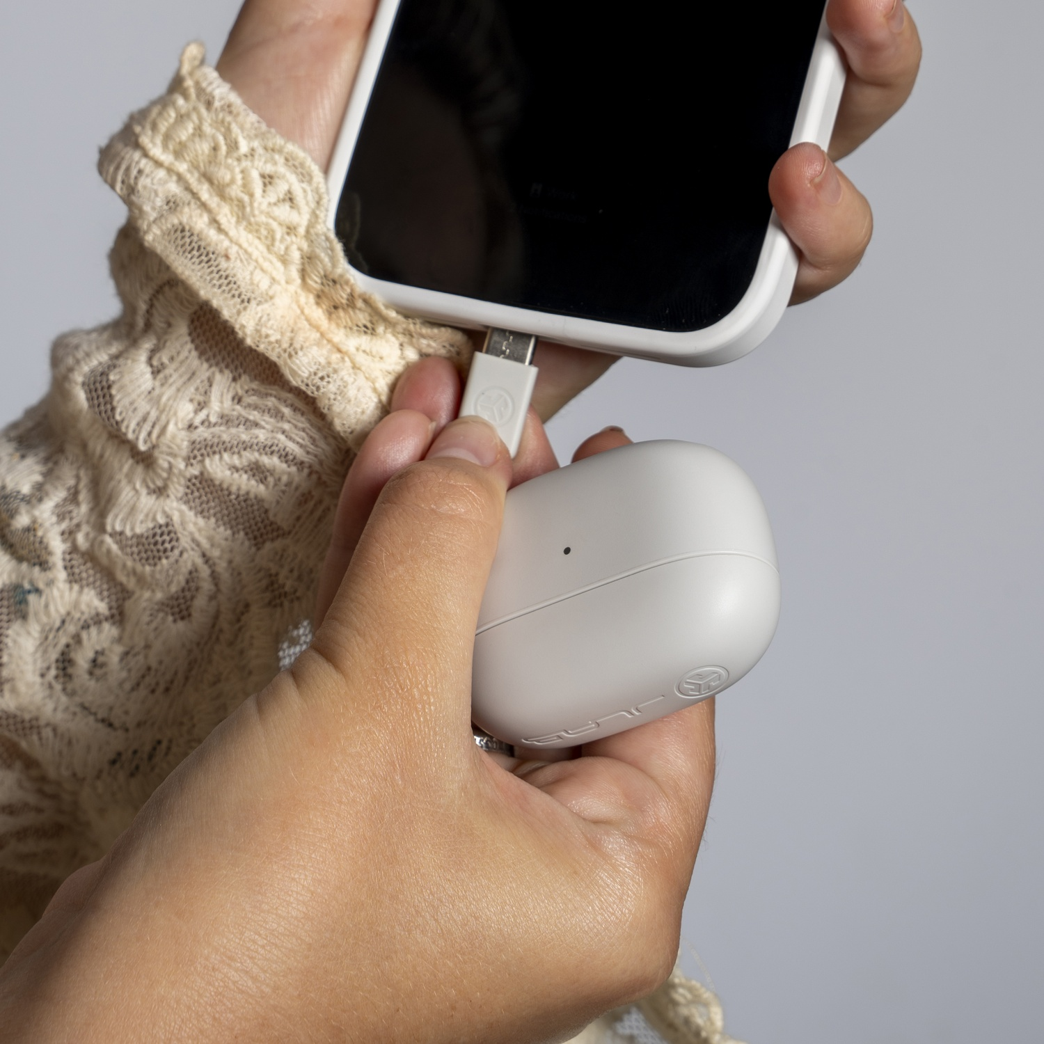 Handen verbinden een witte oplaadkabel met een smartphone en een witte hoes.