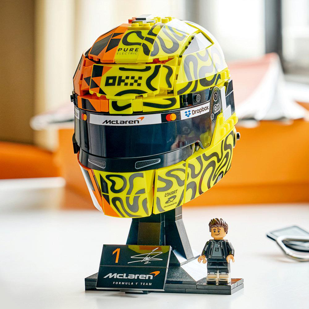 Ein gelber Lego-Helm mit orangen und schwarzen Mustern steht auf einem Ständer.