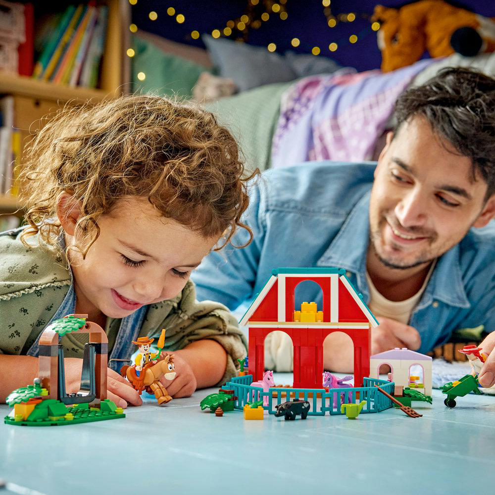 Vater und Kind spielen mit Lego-Bauernhof-Spielzeug auf dem Boden.