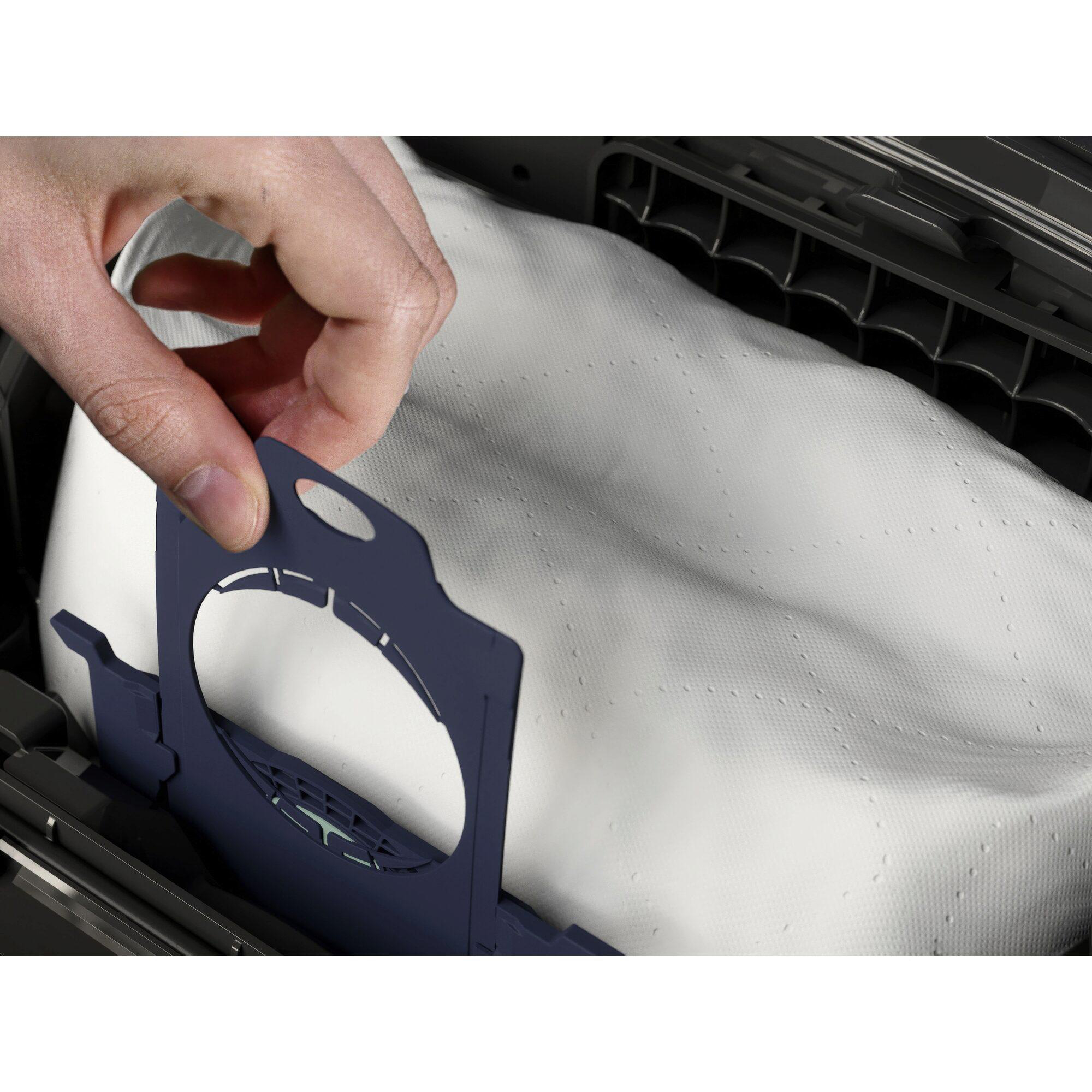 Eine Hand hält einen blauen Adapter über einen weißen Staubsaugerbeutel.